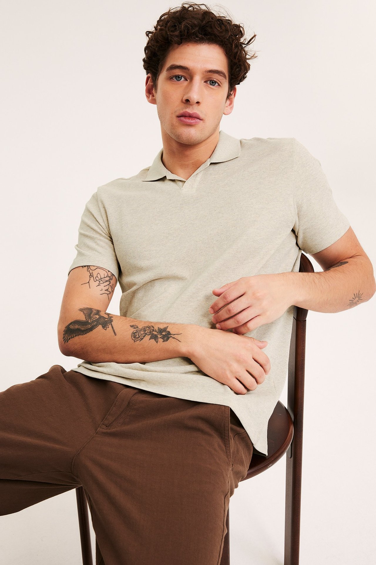 Edestä, mies pukeutuneena beigenkirjavaan puuvillapikeepaitaan ja ruskeisiin housuihin.