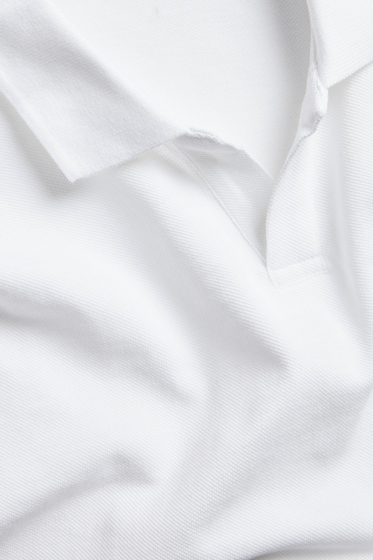 Nærbilde, forfra, av en hvit pikéskjorte i bomull med klassisk krage og åpen knappestolpe.