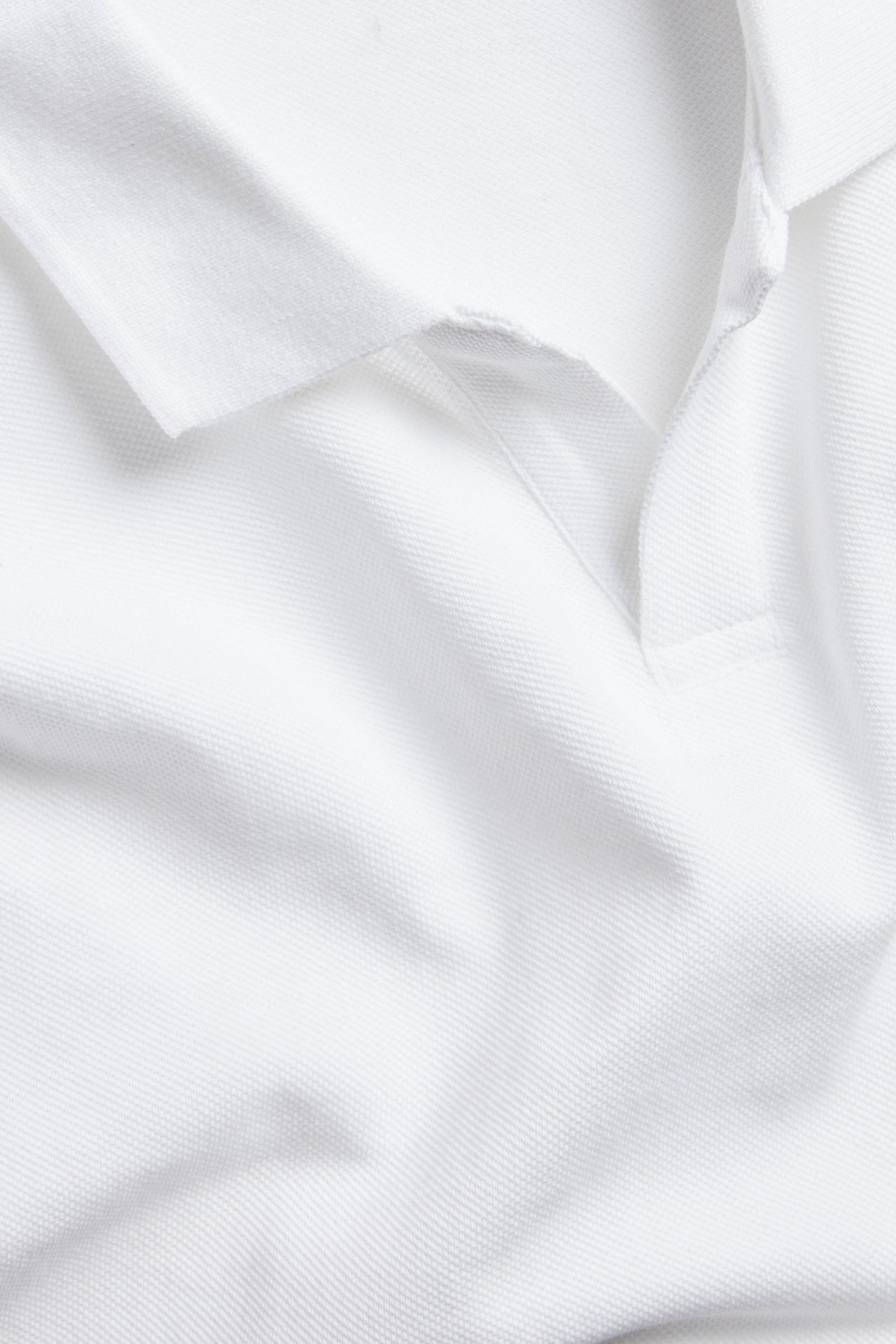 Zbliżenie, przód, białej koszulki polo z bawełny piqué, z klasycznym kołnierzykiem i otwartą listwą.