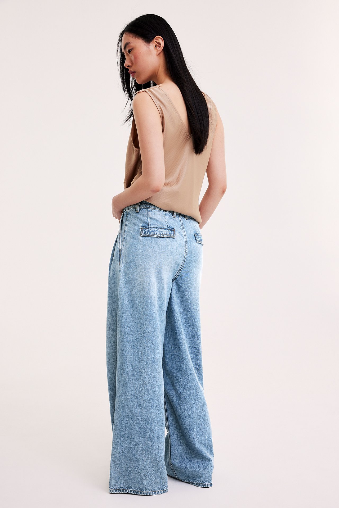 Naisen takavasen kuva, yllään vaaleansiniset leveälahkeiset farkut takataskuläpillä ja beige hihaton toppi.