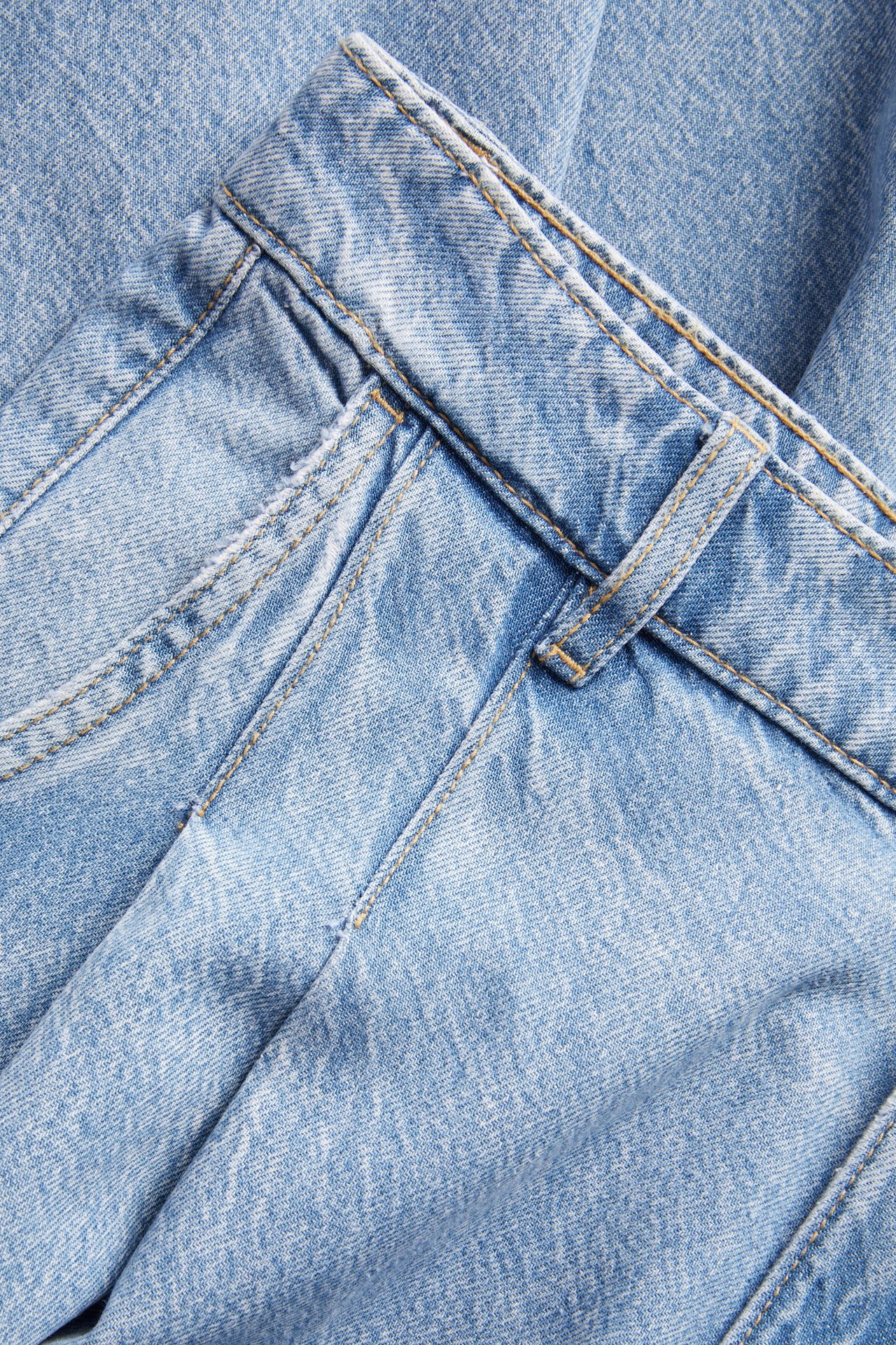 Lähikuva vaaleansinisistä leveistä farkuista, joissa sivutaskut, etulaskokset ja vyötärönauha.