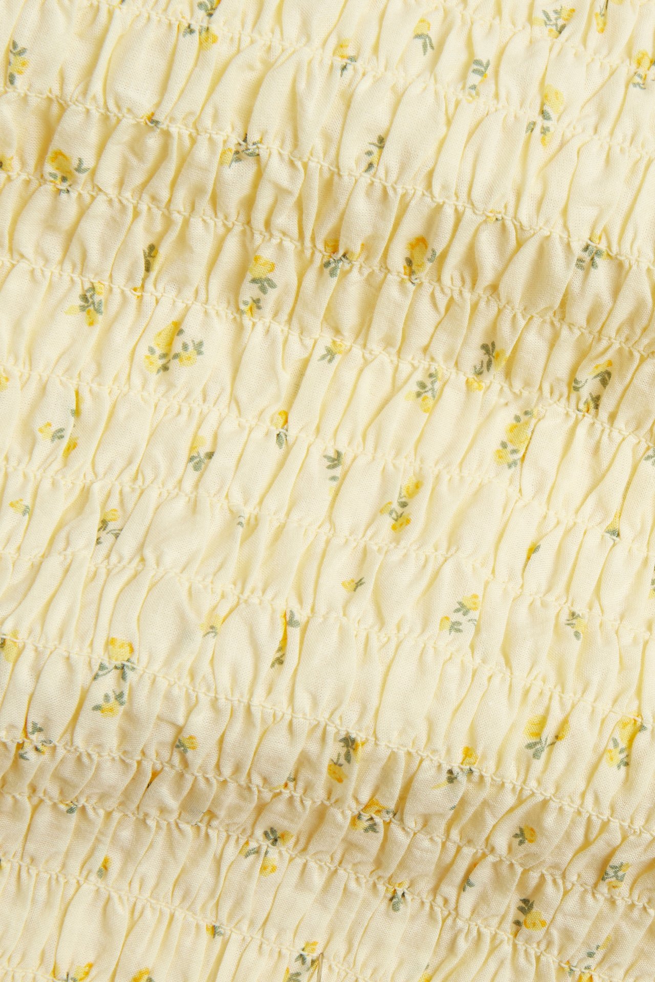 Närbild av en ljusgul smockad bomullstopp med litet blommigt mönster.