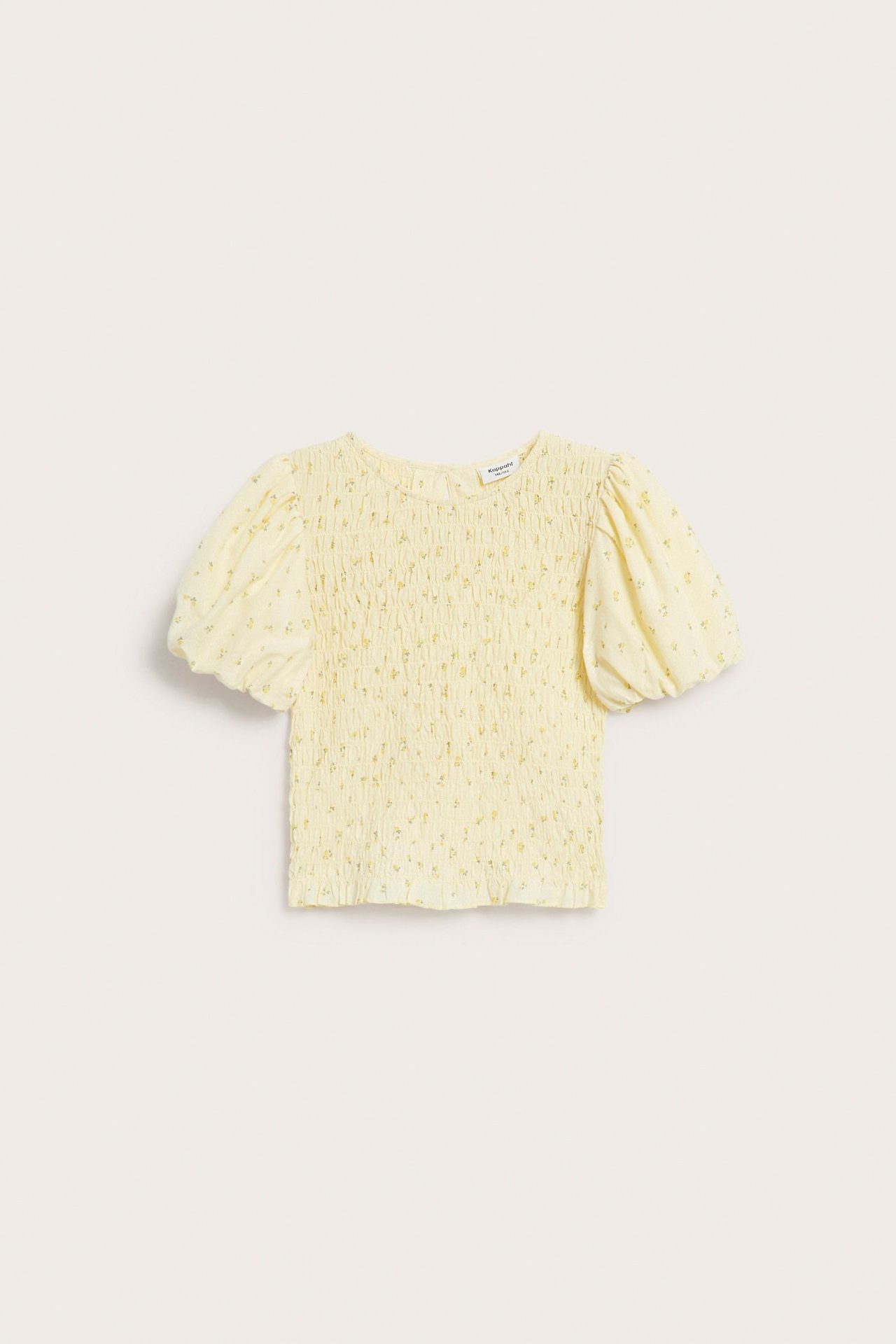 Framifrån syns en ljusgul bomullstopp med smockdetaljer, puffärmar och ett diskret blommönster.