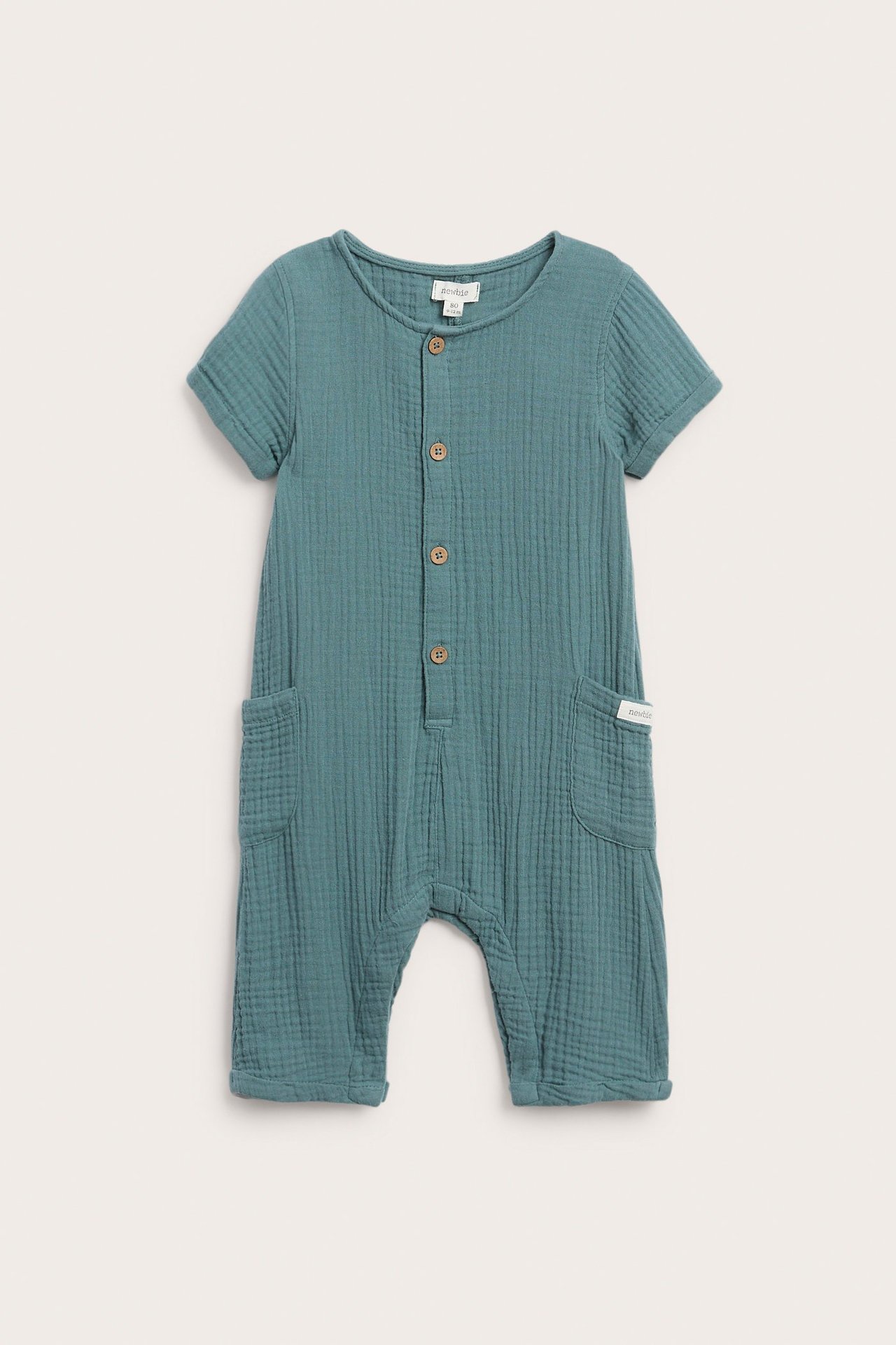 Edestä tummansinivihreä vauvan puuvillamusliinihaalari, jossa lyhyet hihat, napit edessä ja sivutaskut.