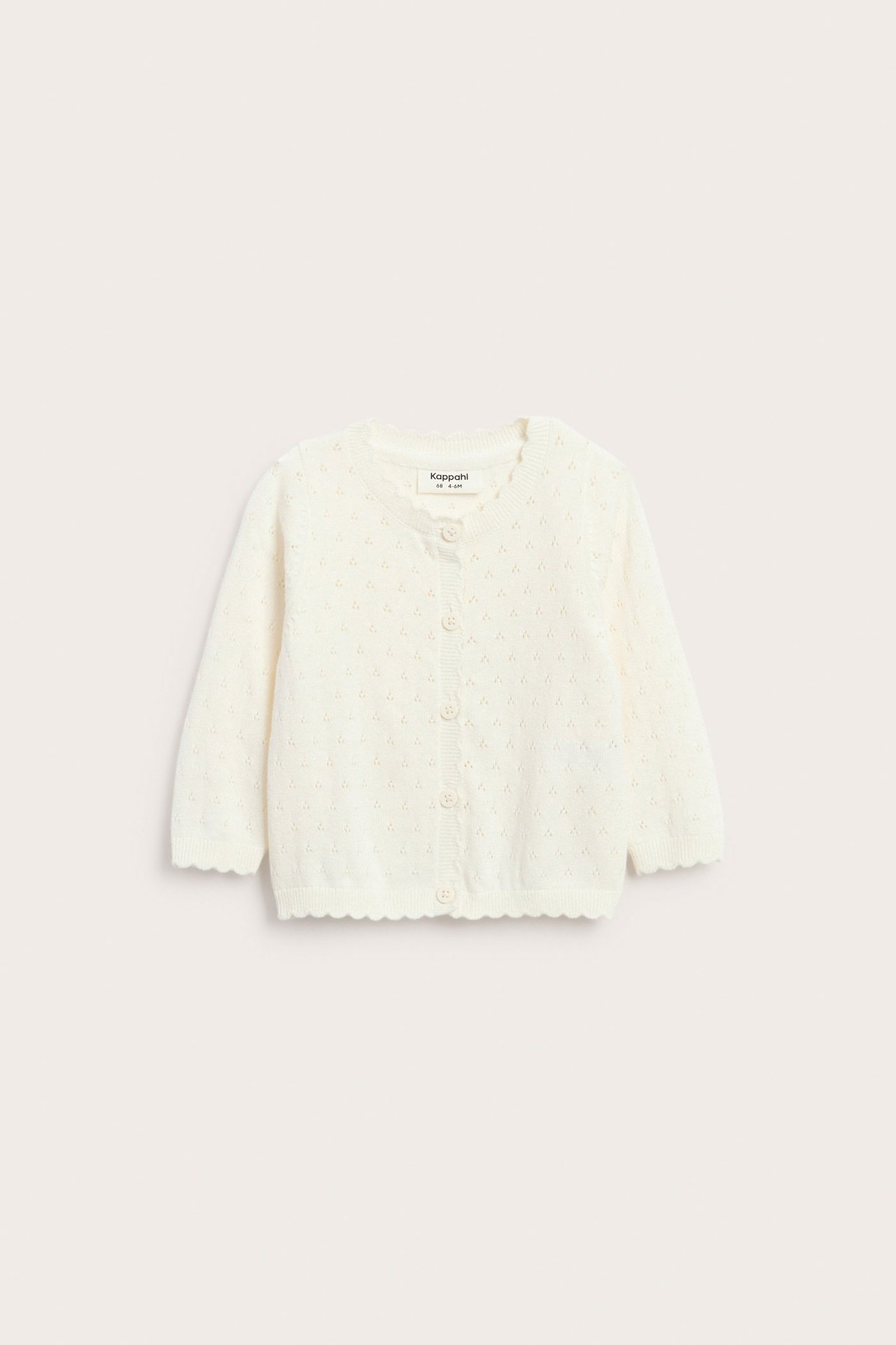 Widok z przodu: ecru sweterek niemowlęcy z bawełny, z ażurowym wzorem i falowanymi brzegami, zapinany na guziki.