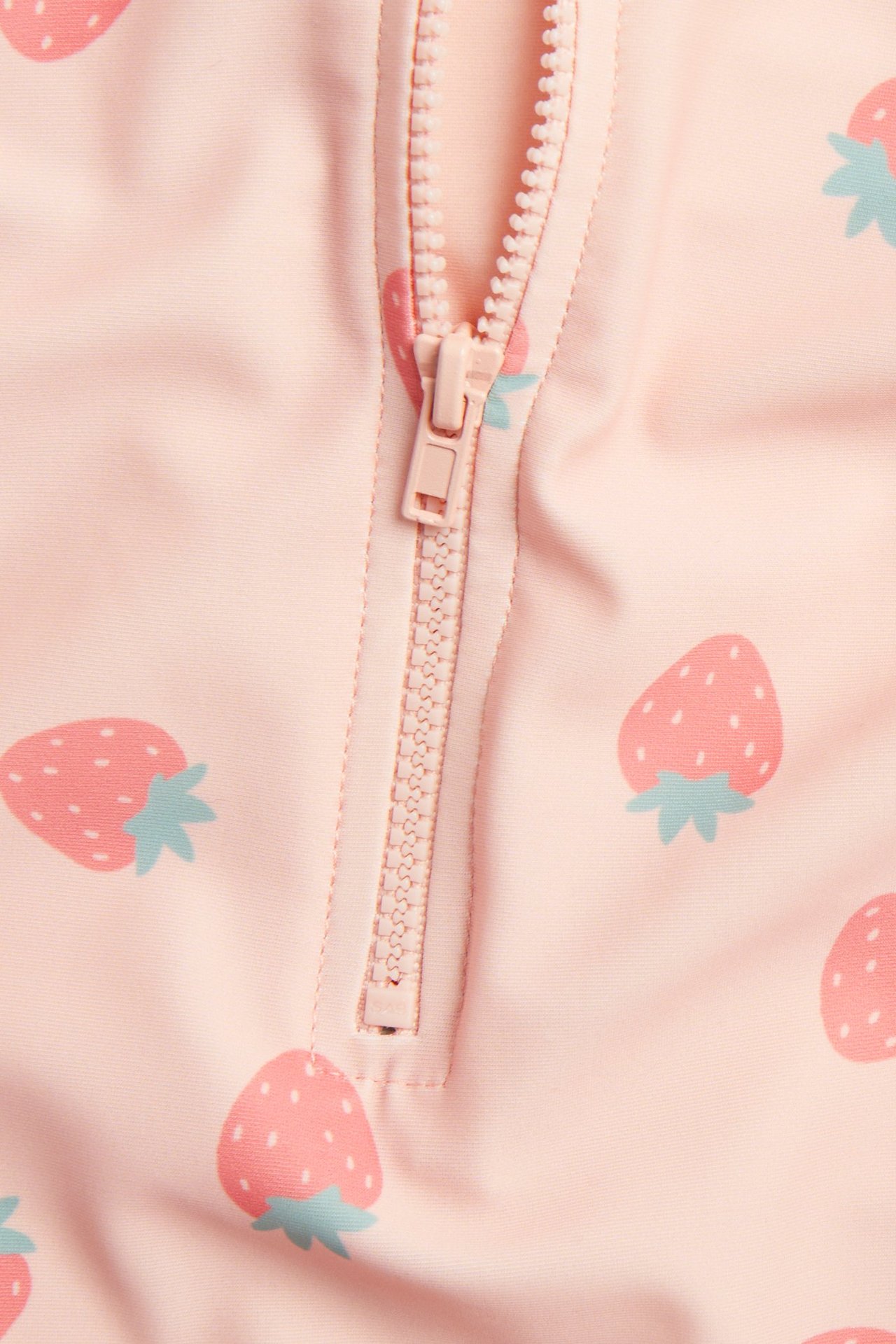 Zbliżenie różowego kombinezonu UV z wzorem truskawek i jasnoróżowym zamkiem błyskawicznym.