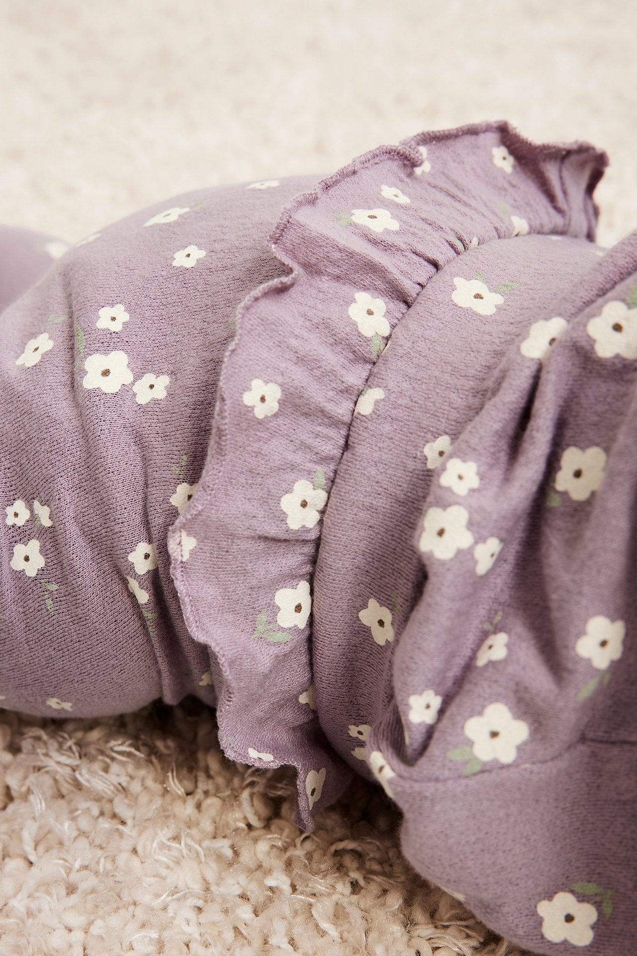 Nærbilde av lilla baby-leggings med hvitt blomstermønster og volanger.