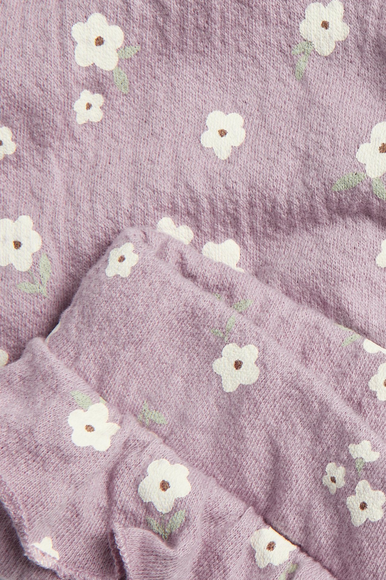 Närbild av lila bomullsblandade blommiga leggings med vitt allover-blomtryck och volangkant.