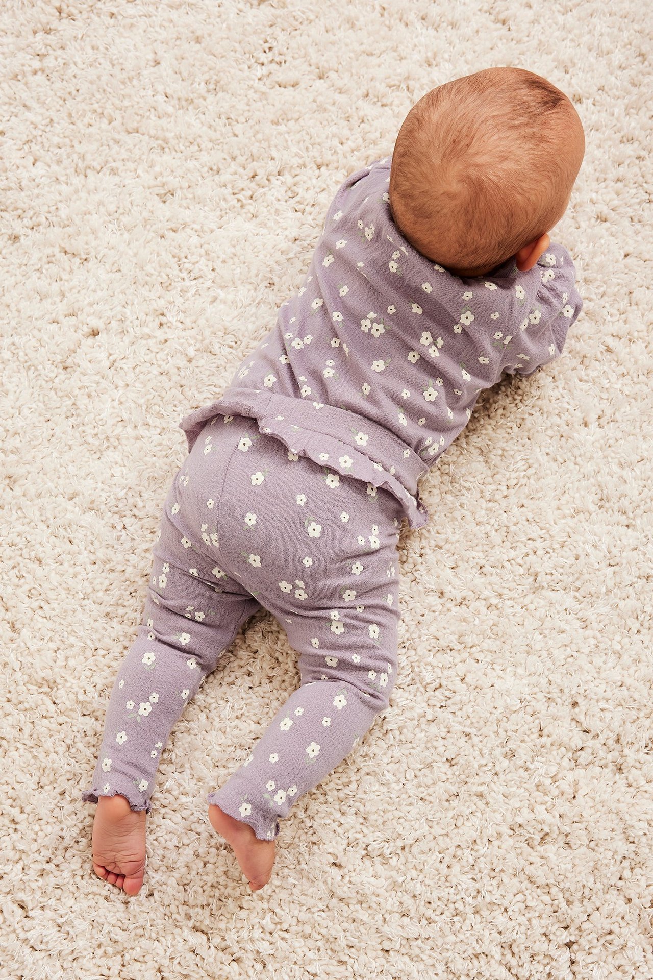 Ovanifrån vy av baby i lila blommiga leggings med volang i midjan och matchande långärmad topp.