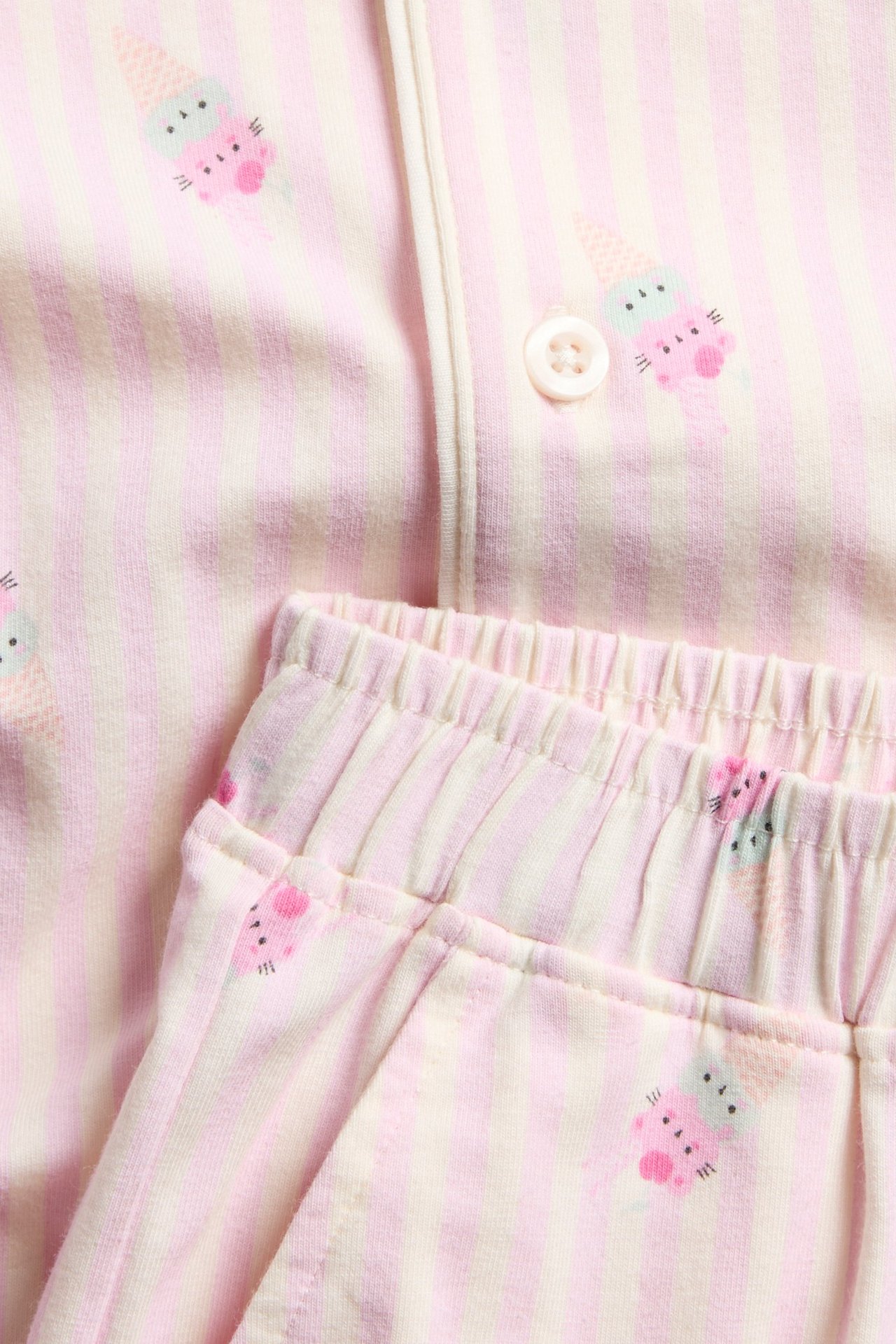 Nærbilde: Barne-pyjamas, off-white og rosa stripete med iskremsmønster, knapp og elastisk midje.