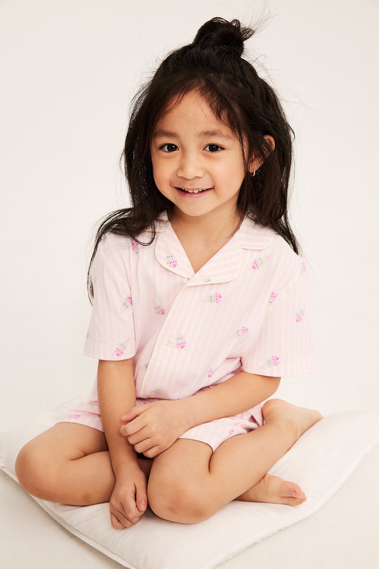 Widok z przodu na dziecko w bawełnianej piżamie w paski off-white i różowe, ze wzorem lodów.