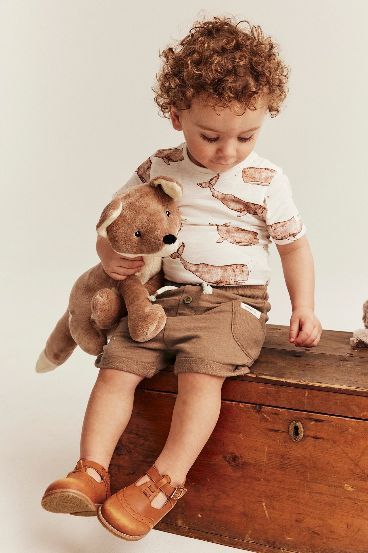 Ruskeat slub-college shortsit kiristysnauhalla lapsella, yhdistettynä valas-t-paitaan ja ruskeisiin kenkiin.
