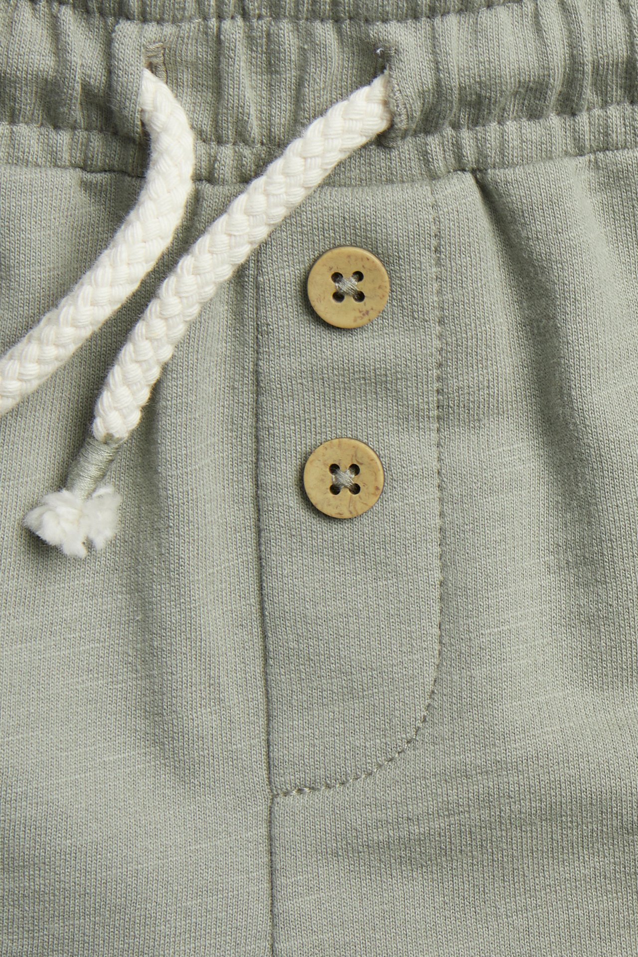 Zbliżenie na ciemnozielone szorty slub: elastyczna talia, biały sznurek, ozdobne brązowe guziki.