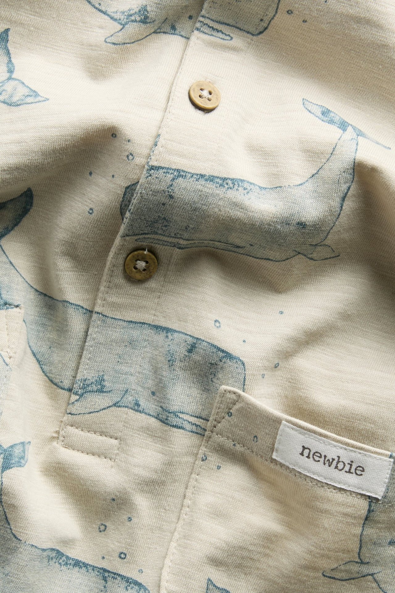 Widok z przodu z bliska beżowego bawełnianego rompera w niebieskie wieloryby z brązowymi guzikami.