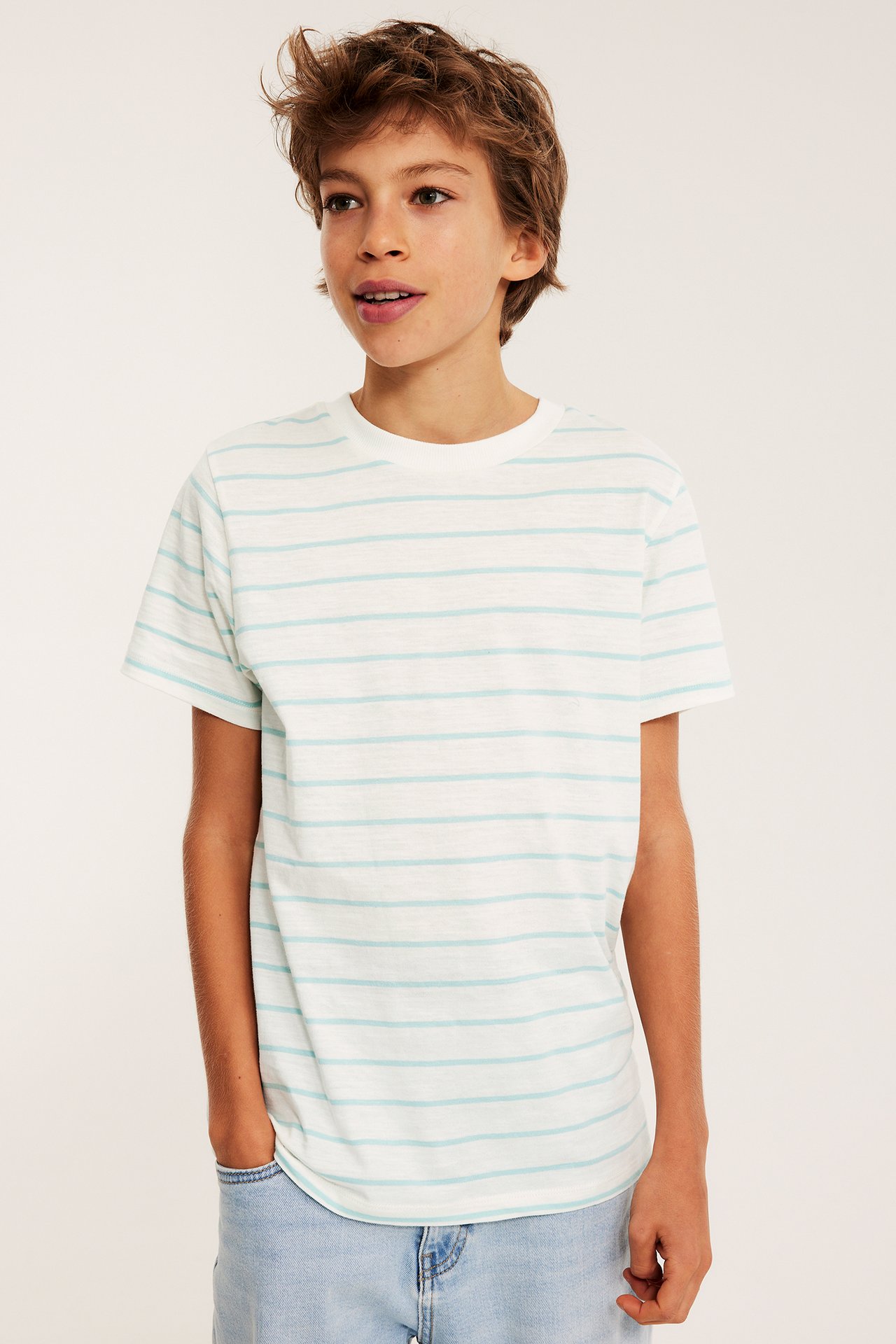Edestäpäin, lapsi valkoisessa raidallisessa puuvilla t-paidassa, jossa vaaleansiniset raidat ja vaaleansiniset farkut.