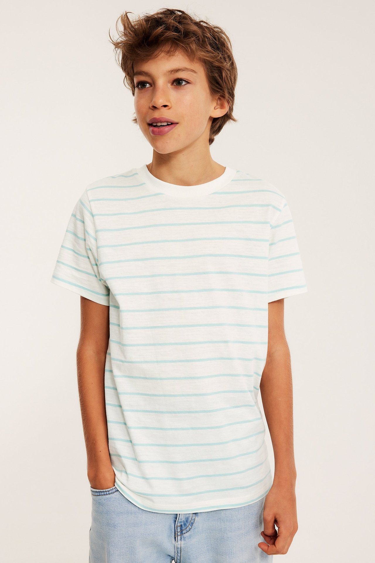 Edestäpäin, lapsi valkoisessa raidallisessa puuvilla t-paidassa, jossa vaaleansiniset raidat ja vaaleansiniset farkut.