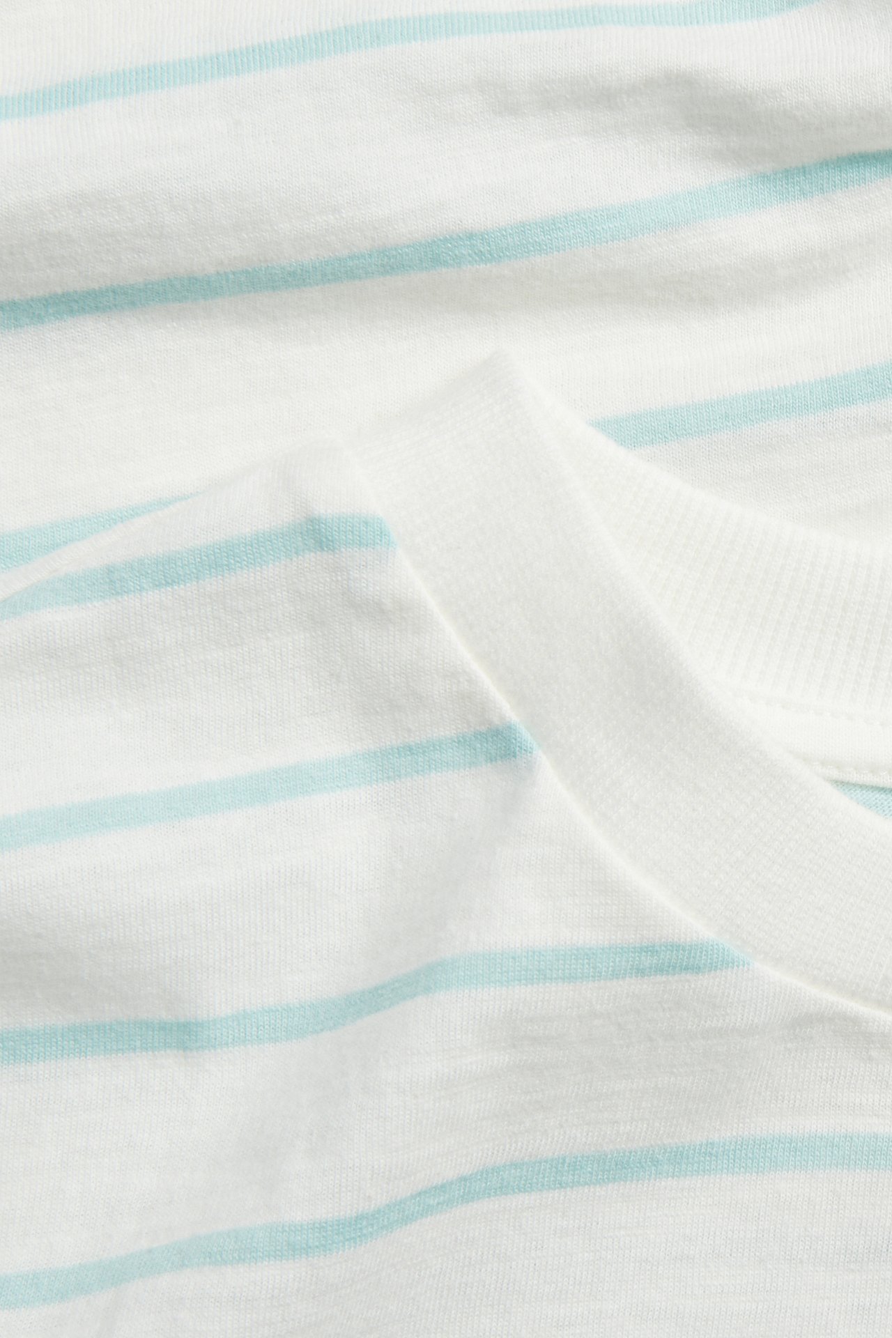 Zbliżenie na białą bawełnianą koszulkę z jasnoturkusowymi paskami i prążkowanym dekoltem.