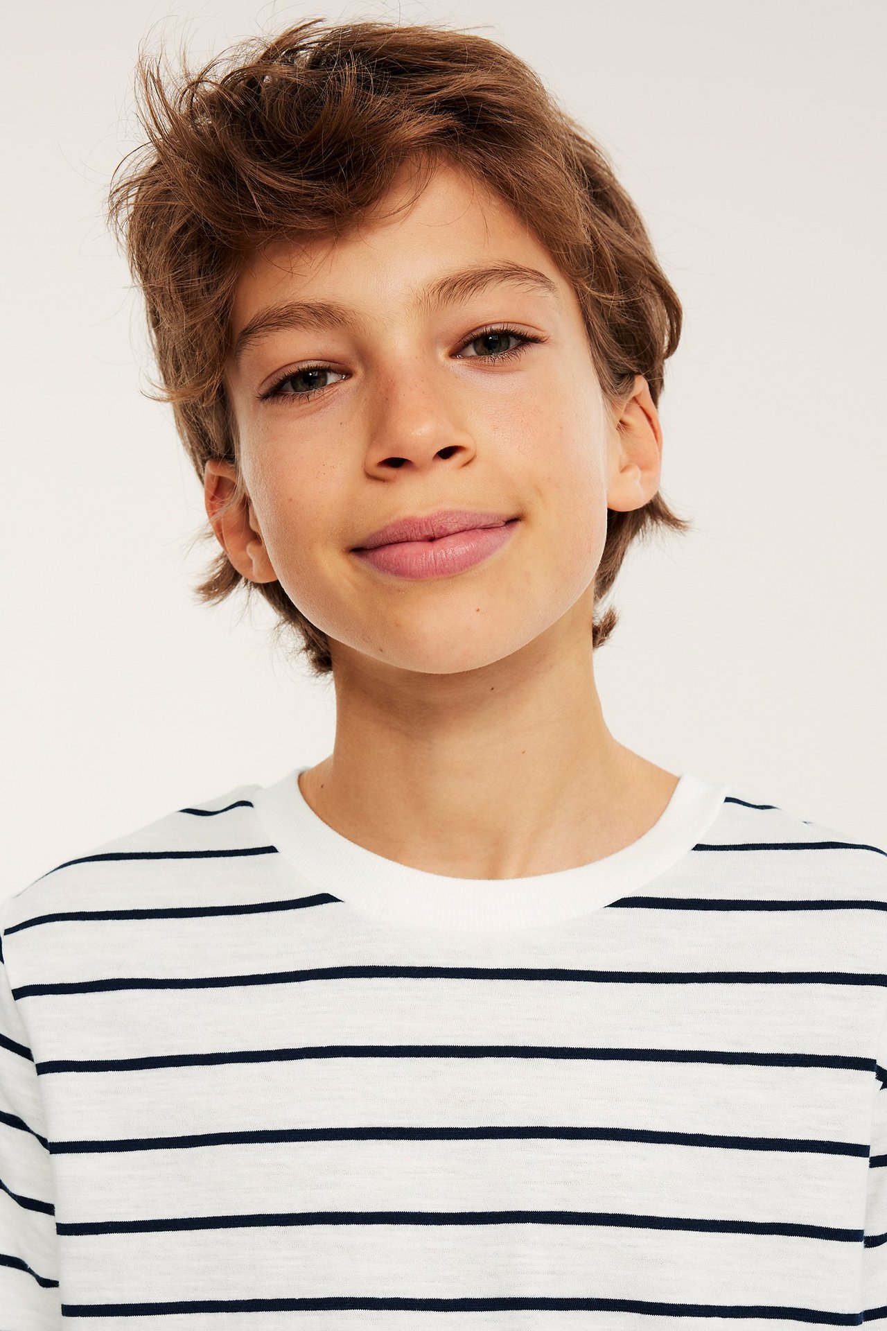 Nærbilde forfra: barn har på seg en hvit bomullsslub T-skjorte med mørkeblå striper og ribbet rund hals.