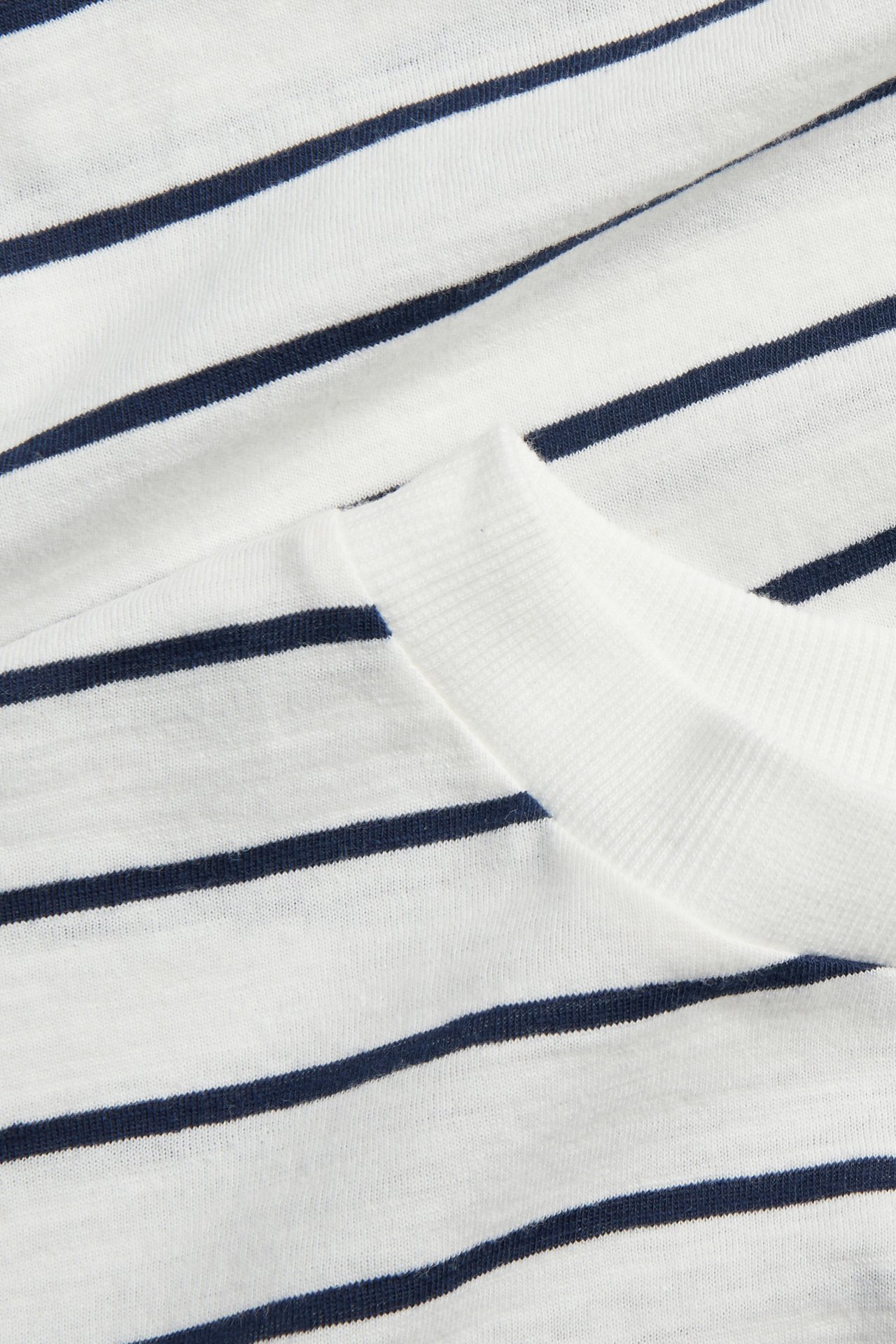 Zbliżenie na białą bawełnianą koszulkę w granatowe paski z prążkowanym dekoltem.