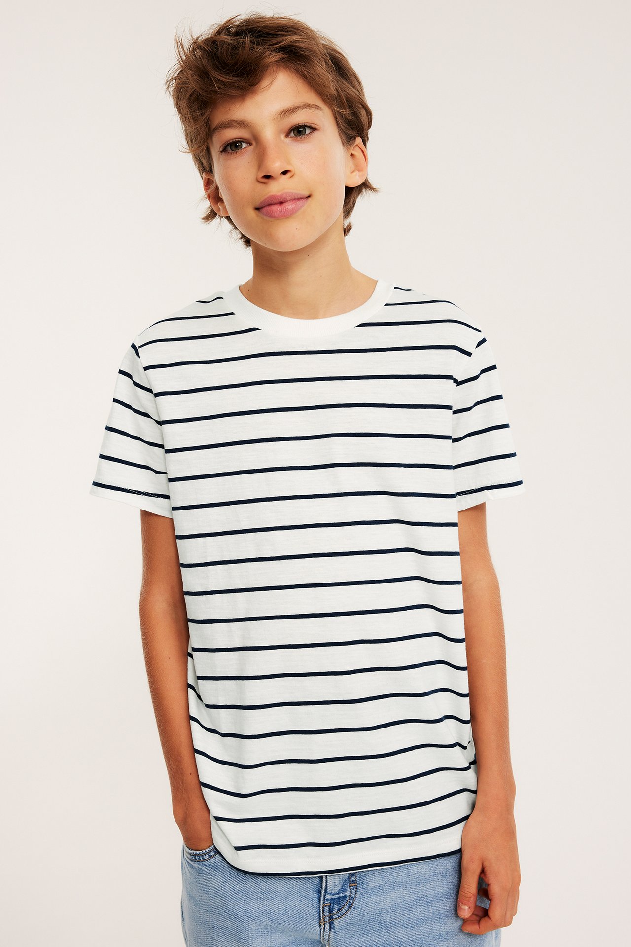 Widok z przodu: dziecko w białym bawełnianym T-shircie w granatowe paski i jasnych jeansach.