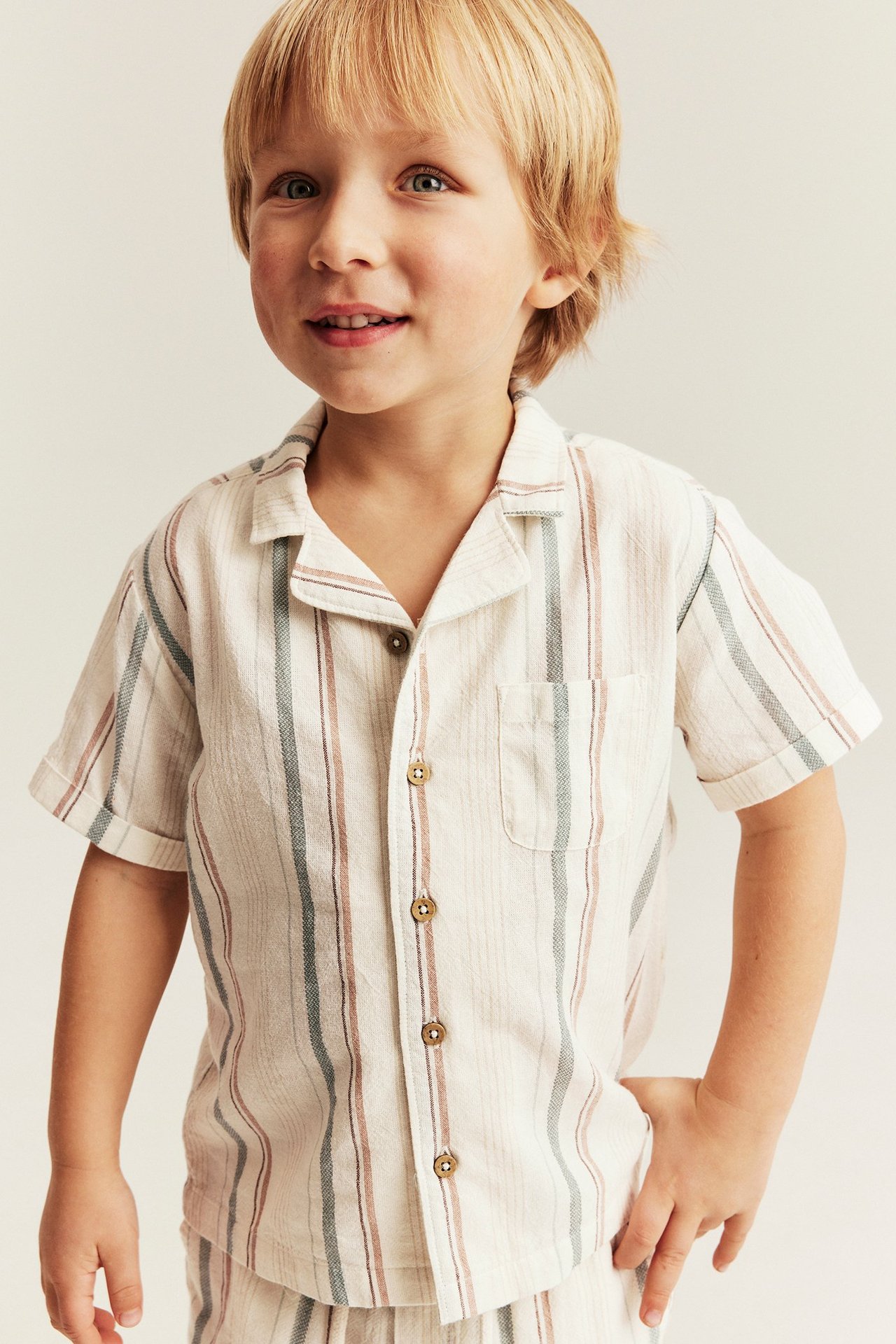 Widok z przodu dziecka w pasiastym, krótkim, bawełnianym koszuli off-white i pasujących szortach.