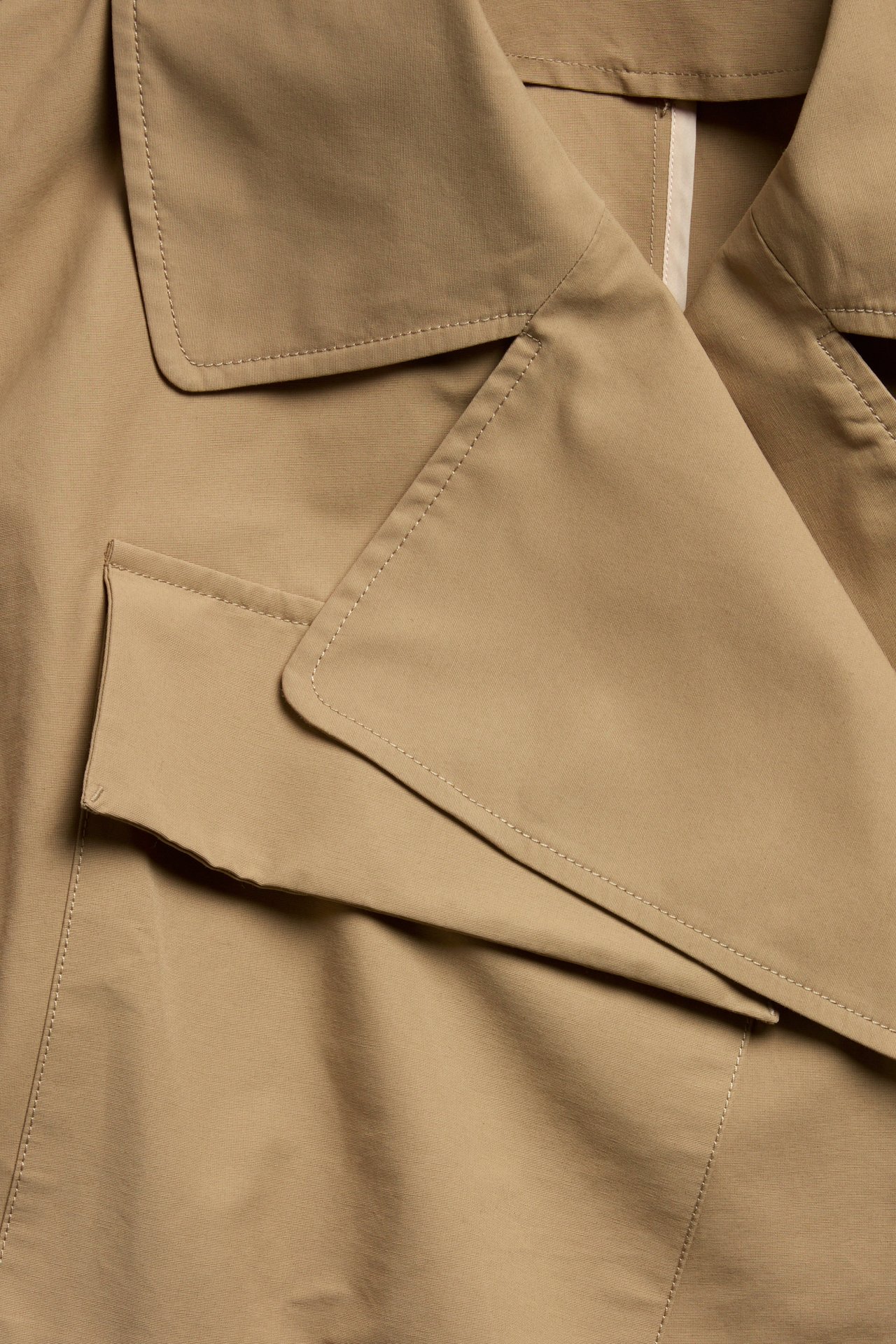 Närbild av en beige trenchcoat i bomullsblandning med bred krage och synlig ficklock.