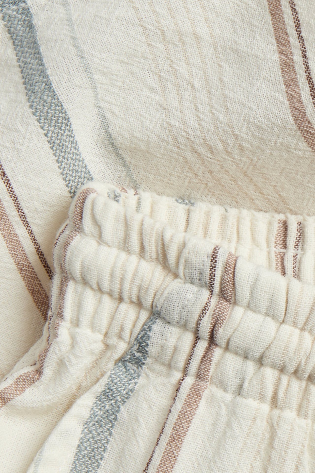 Zbliżenie na off-white tkane szorty w paski z elastyczną talią i brązowymi, niebieskimi paskami.