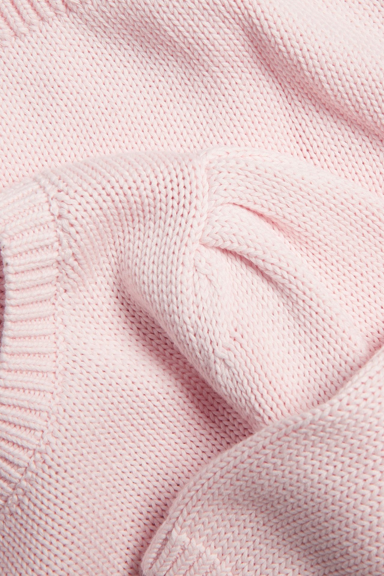 Zbliżenie jasnoróżowego grubego bawełnianego swetra z bufiastymi rękawami.
