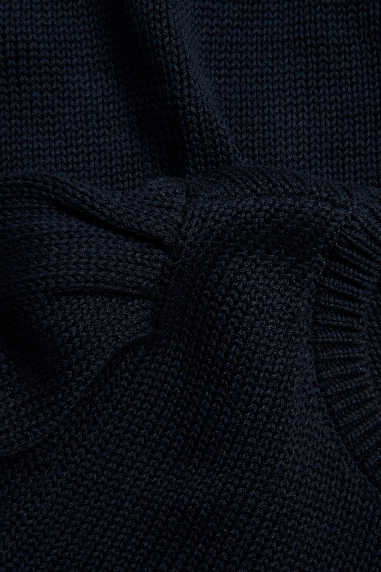 Lähikuva tummansinisestä paksusta puuvillaneulepuserosta, jossa näkyvä neulosrakenne ja hienovarainen puhvihihayksityiskohta.