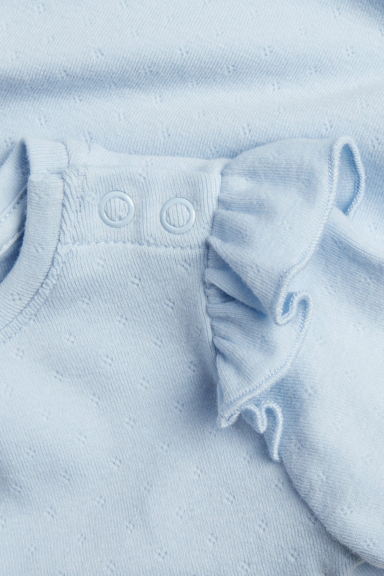 Zbliżenie: jasnoniebieskie body niemowlęce pointelle z długimi rękawami, falbankami i zatrzaskami.