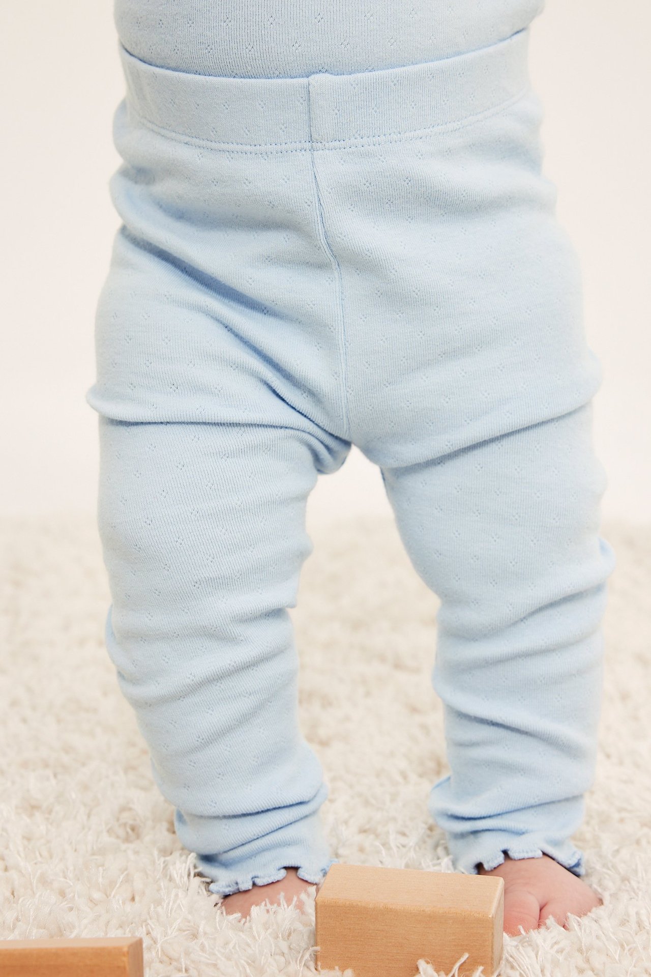 Från framsidan, ljusblå pointelle baby leggings med resår i midjan och baby lock-fållar.