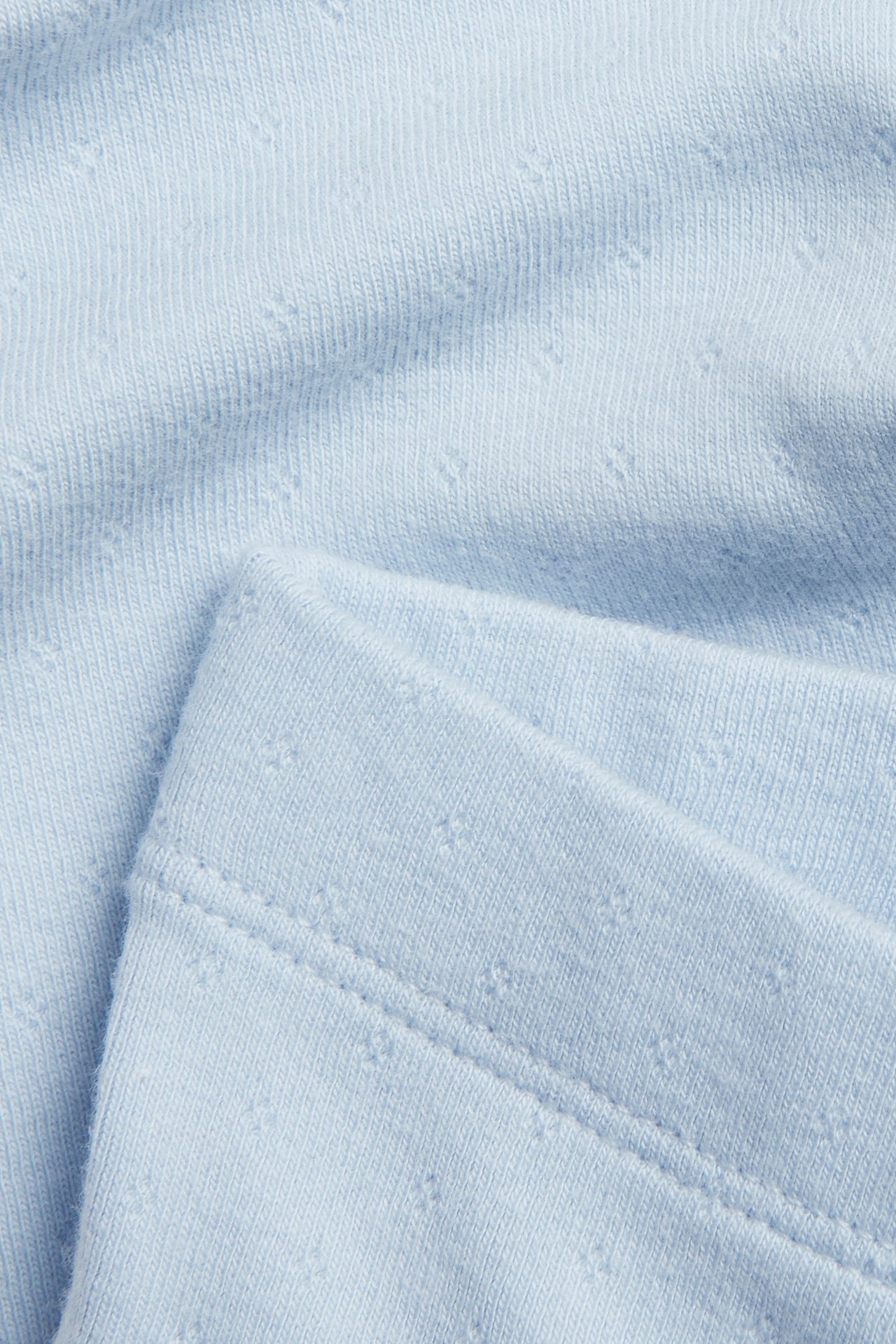 Zbliżenie na jasnoniebieskie legginsy niemowlęce z wzorem pointelle i widocznym szwem.