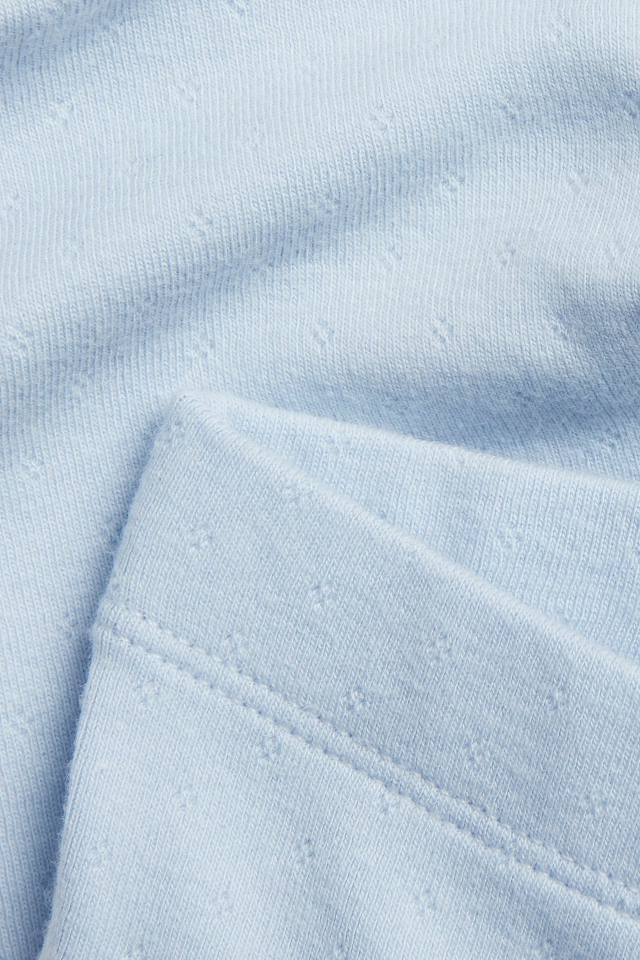 Zbliżenie na jasnoniebieskie legginsy niemowlęce z wzorem pointelle i widocznym szwem.