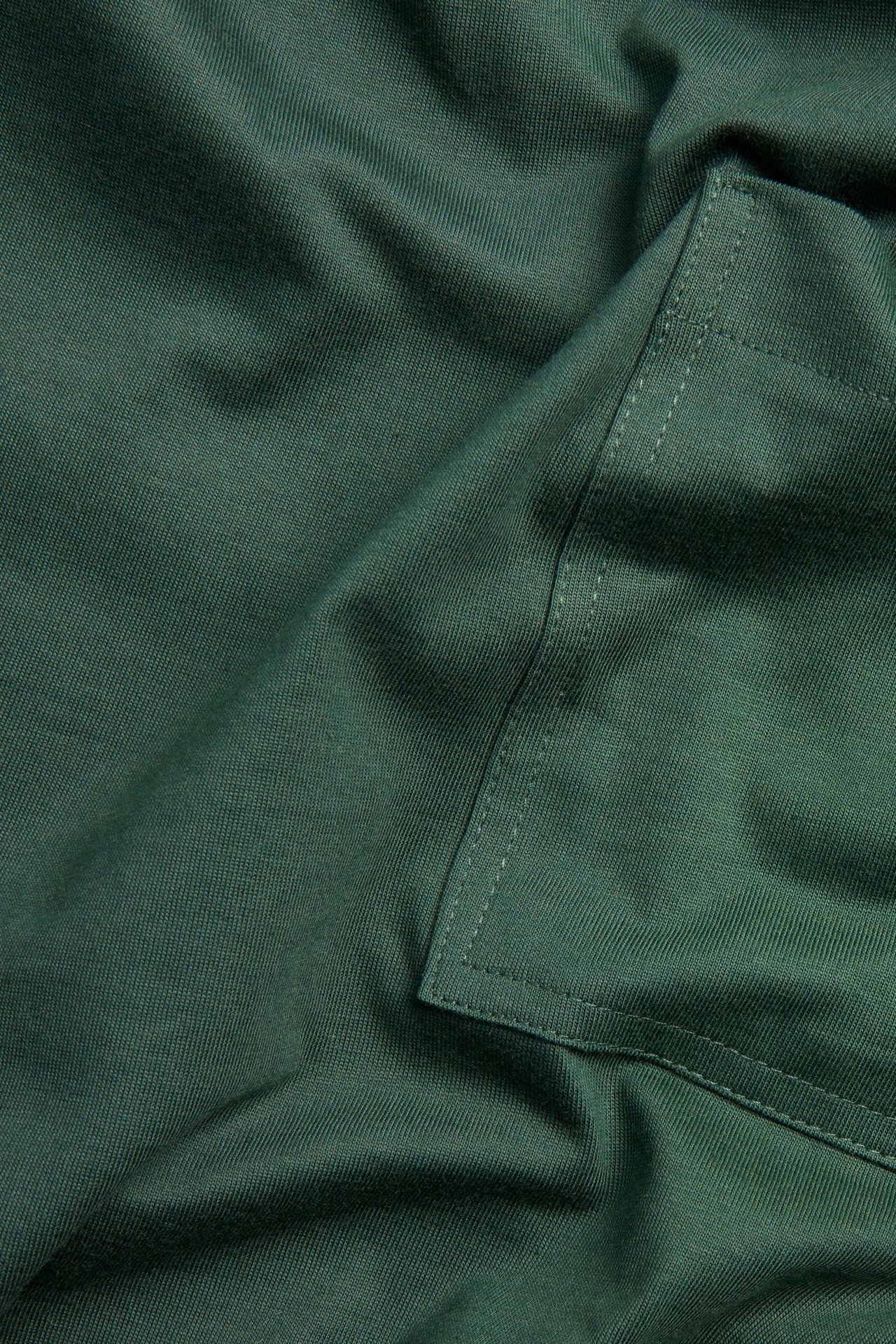 Zbliżenie zielonej, bawełnianej tkaniny T-shirta z widoczną kieszonką na piersi.