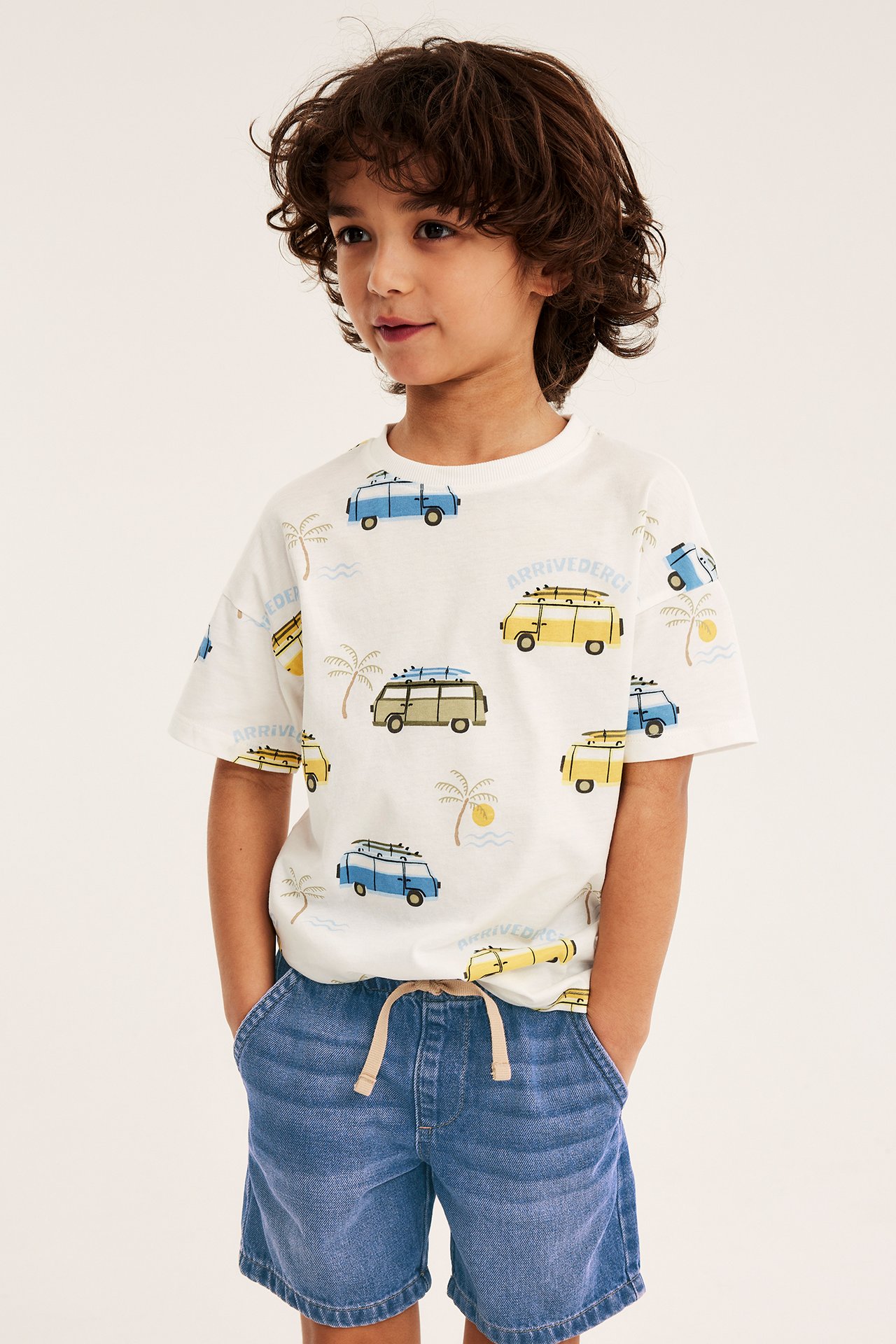 Framifrån, ett barn i mörkblå dra-på-jeansshorts med dragsko och en vit mönstrad t-shirt.