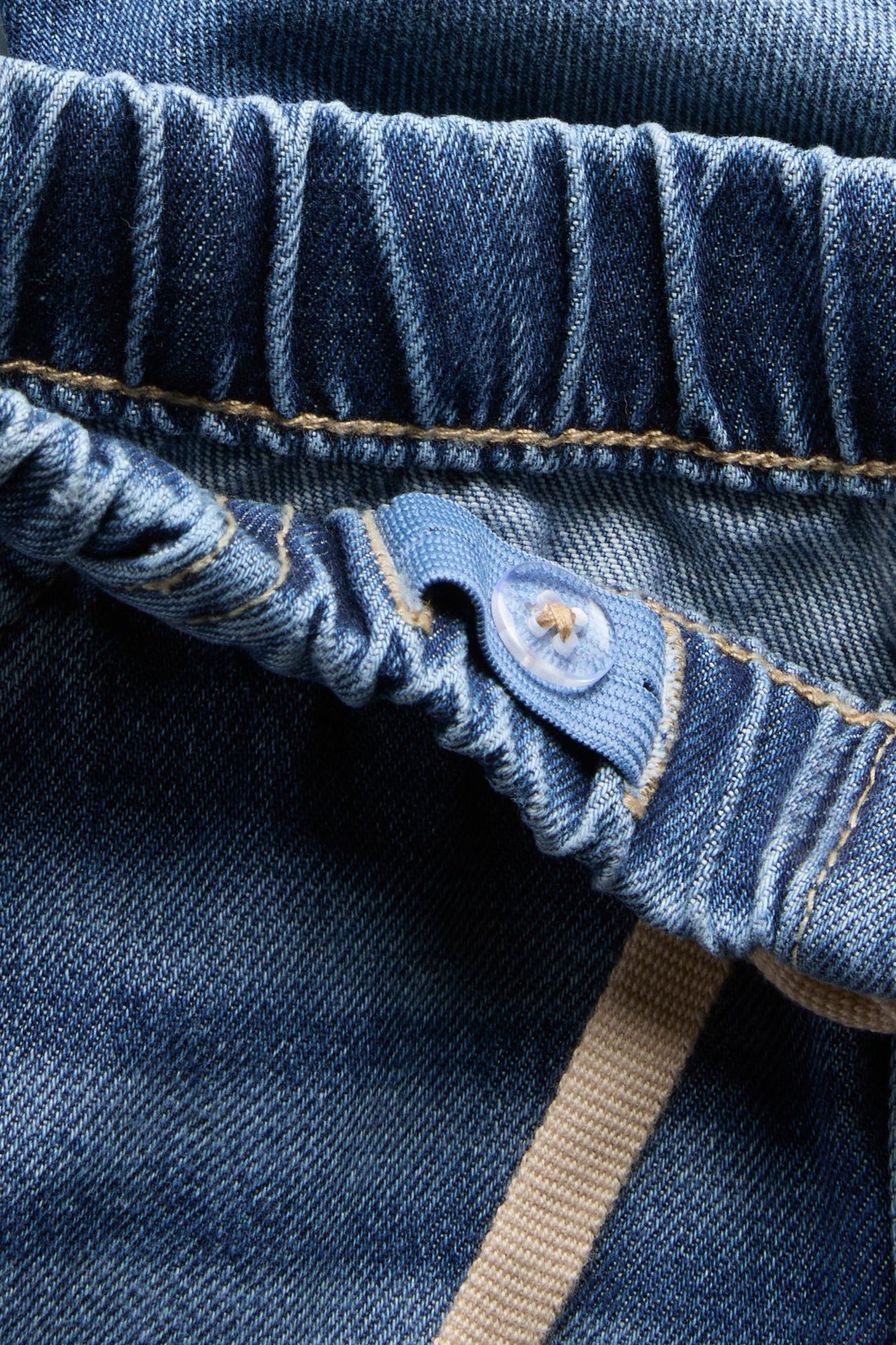 Zbliżenie ciemnoniebieskich jeansowych szortów z elastyczną talią i wewnętrzną regulacją na guzik.