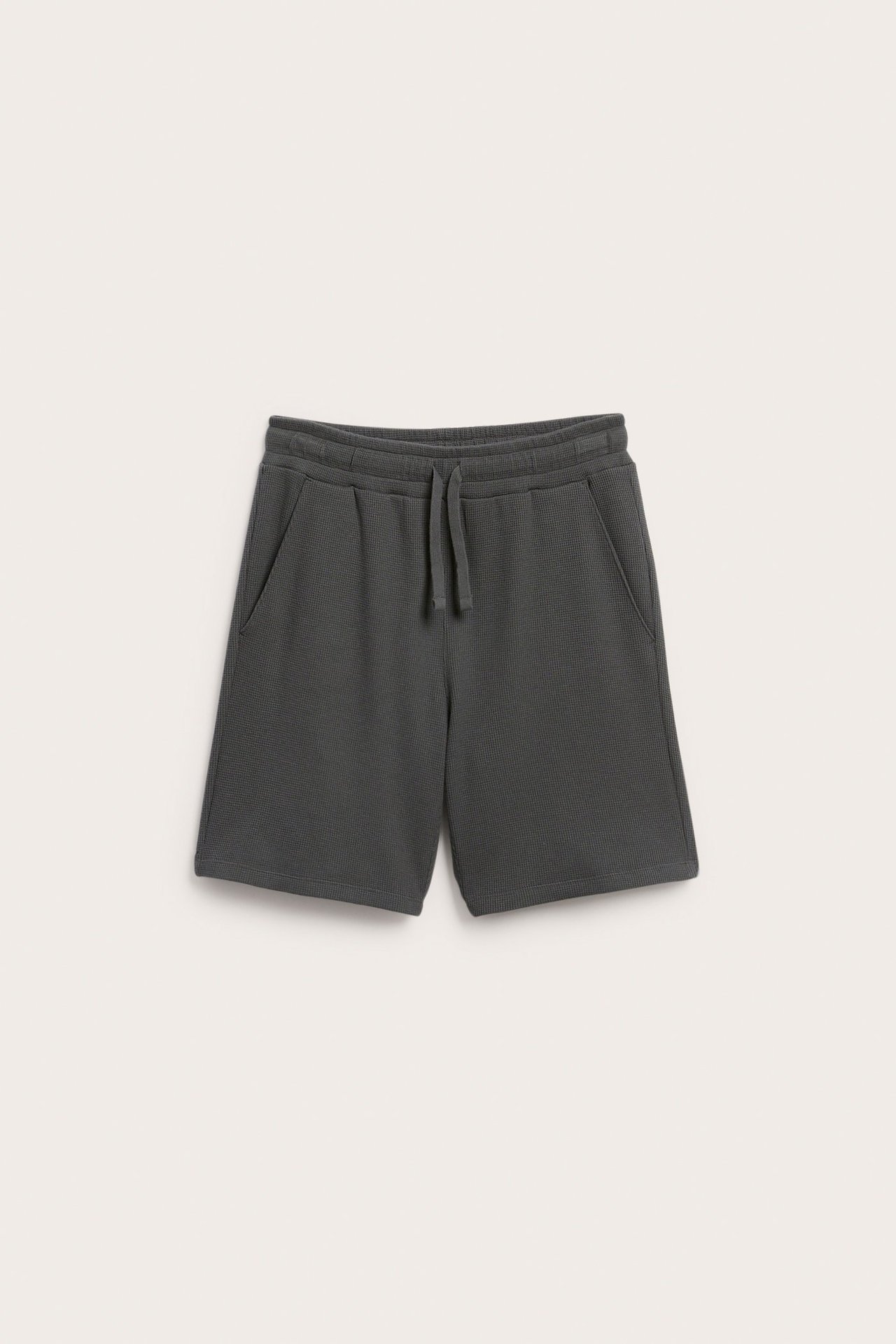 Edestä: Tummanharmaat vohvelikuvioiset puuvillashortsit, joissa kuminauhavvyötärö, kiristysnyöri ja sivutaskut.