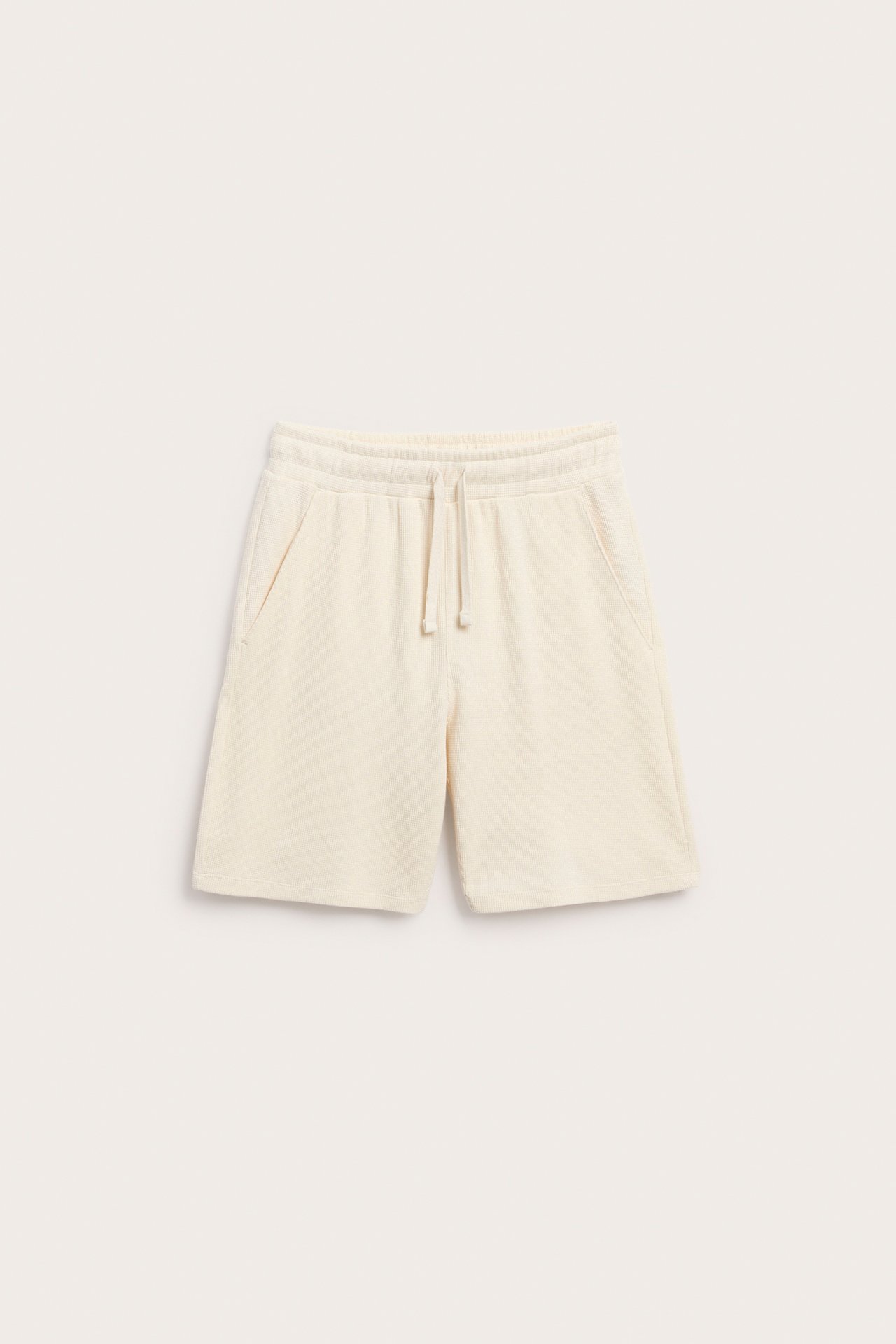 Frontvisning av lys beige vaffelbomullsshorts med elastisk snøring i midjen og sidelommer.
