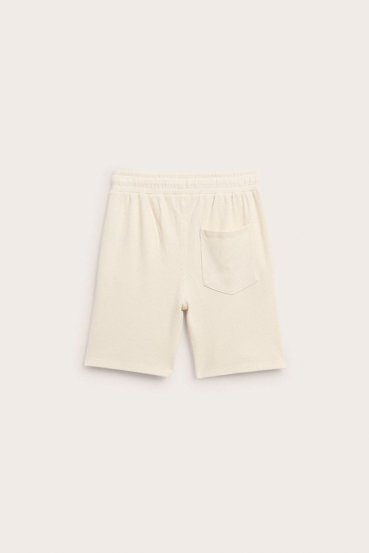 Bakfra: lysebeige vaffelstrikkede bomullsshorts med elastisk midje og en baklomme.