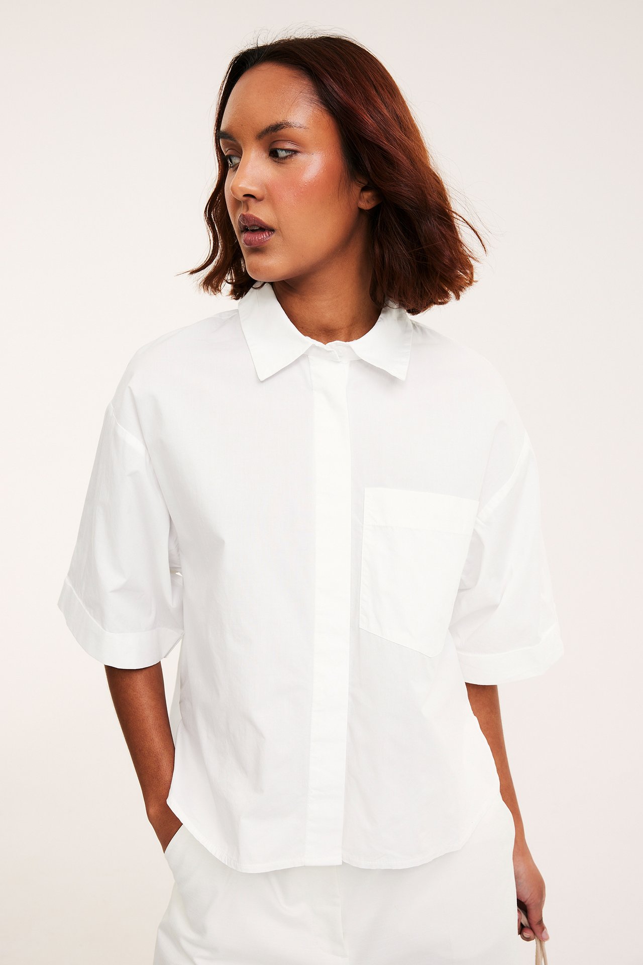 Forfra, kvinne i hvit kortermet bomullspoplin-skjorte med brystlomme.