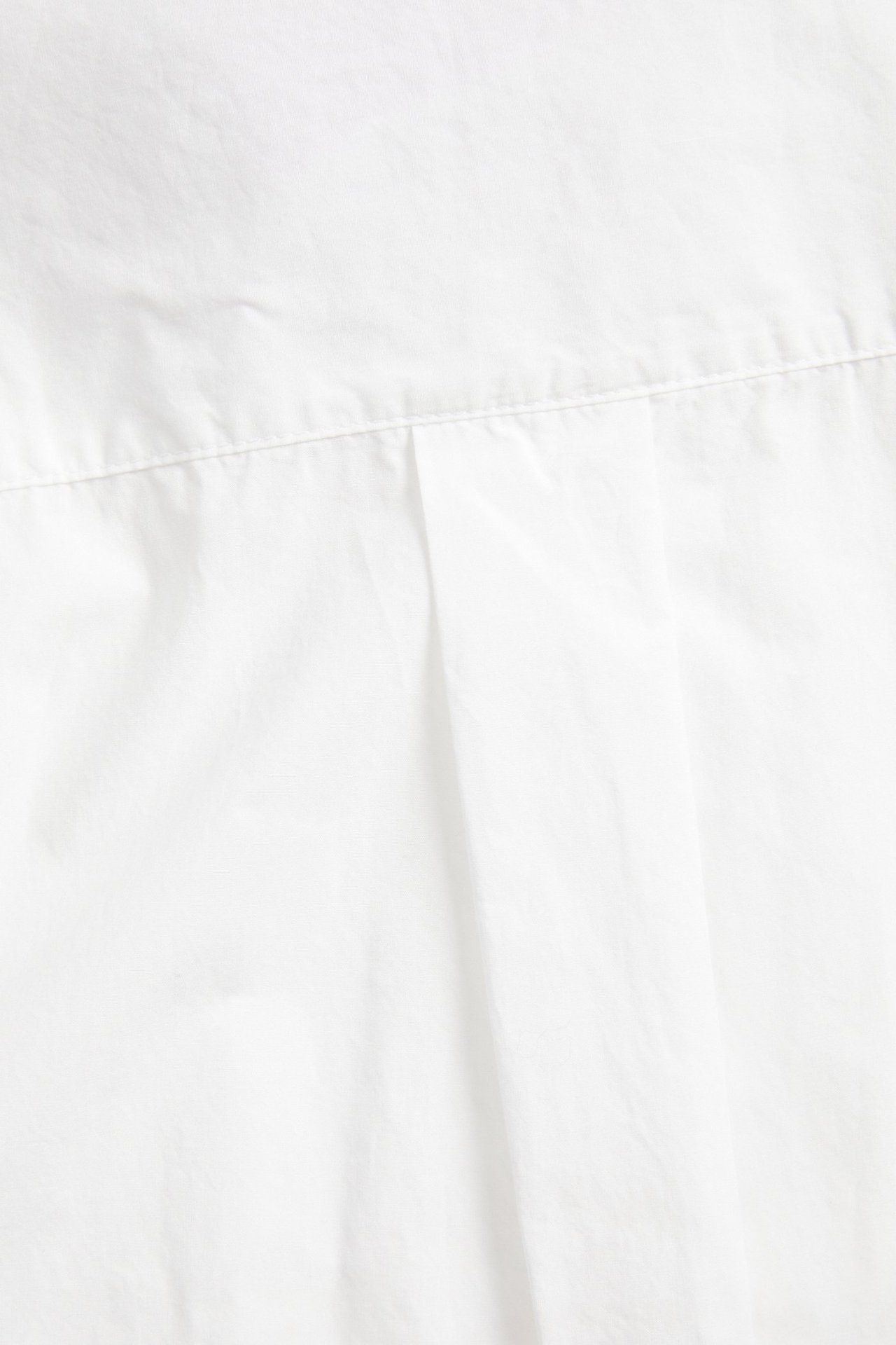 Nærbilde av hvit bomullspoplin skjortestoff, med søm og legg.