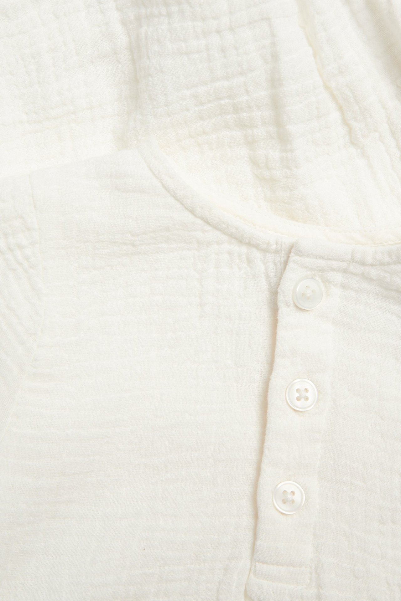 Lähikuva luonnonvalkoisesta pitkähihaisesta muslin-vauvanbodysta kolmella valkoisella paitanaapilla edessä.