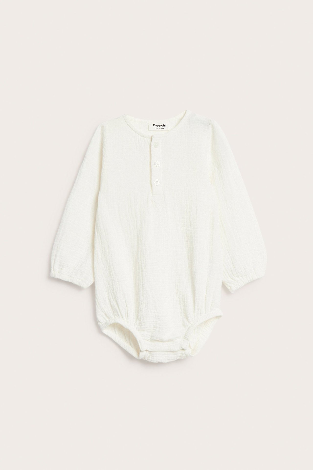 Edestäpäin, luonnonvalkoinen pitkähihainen vauvan musliinihaalari paitanapeilla ja neppareilla.