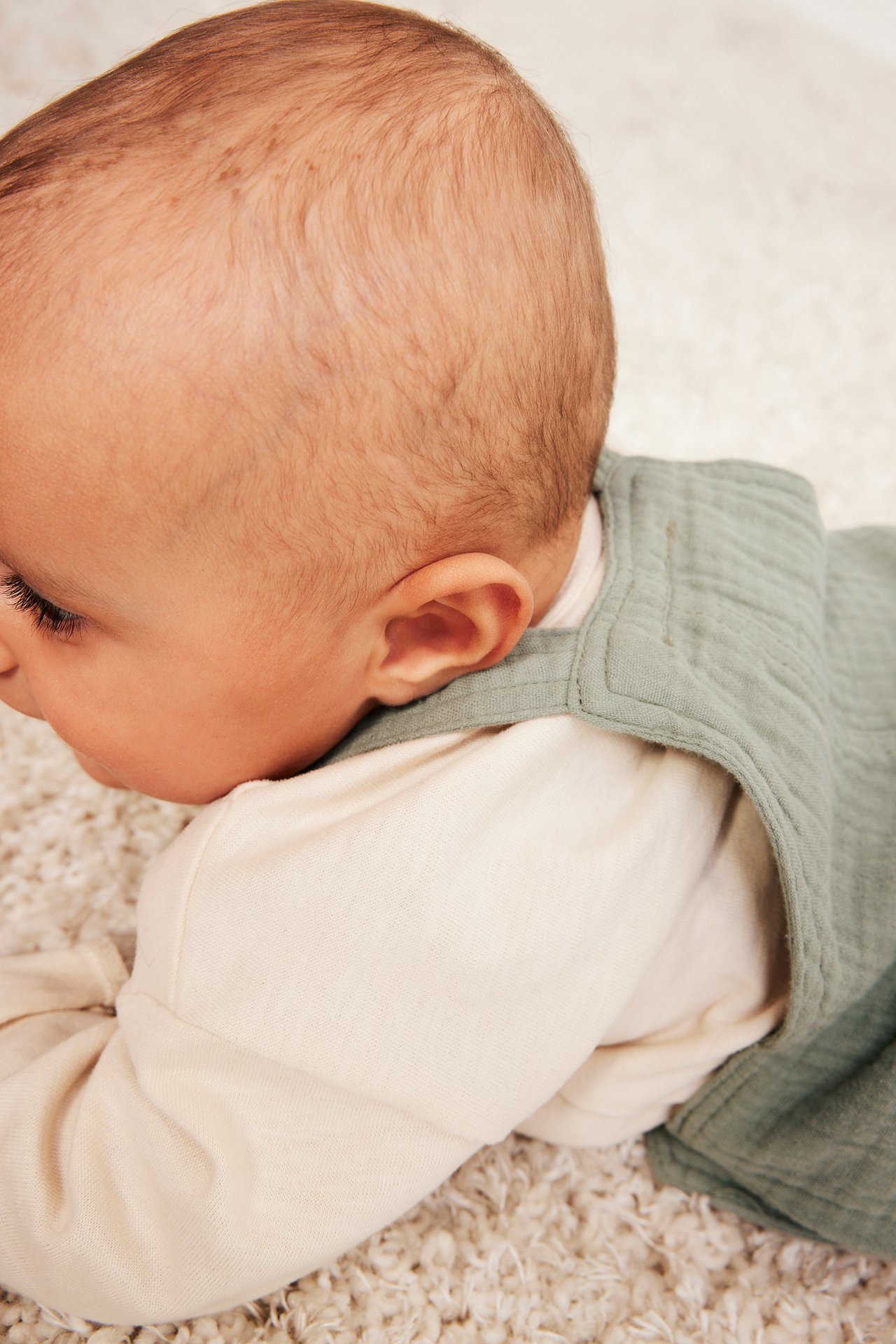 Lähikuva, sivukuva vauvasta yllään tummanvihreät rypistetyt musliinihaalarit vaalean beigen pitkähihaisen paidan päällä.