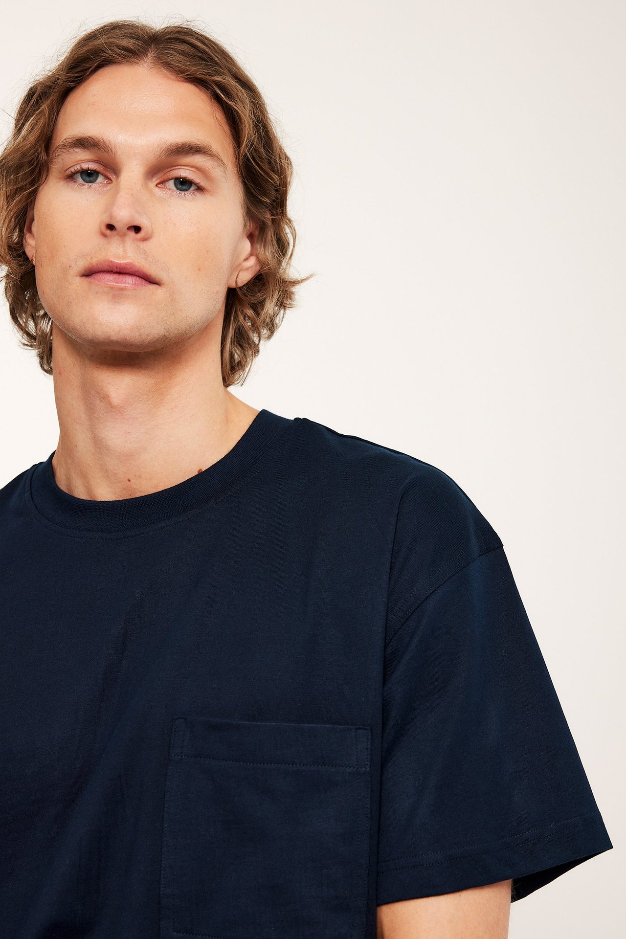 Närbild framifrån på en man i en mörkblå, lös bomulls-T-shirt med bröstficka.