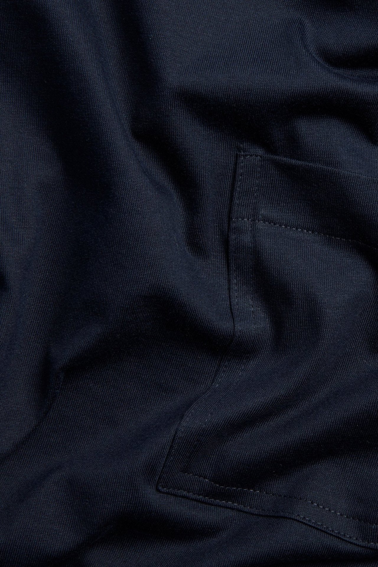 Lähikuva tummansinisestä löysästä puuvilla T-paidasta, jossa rintatasku.