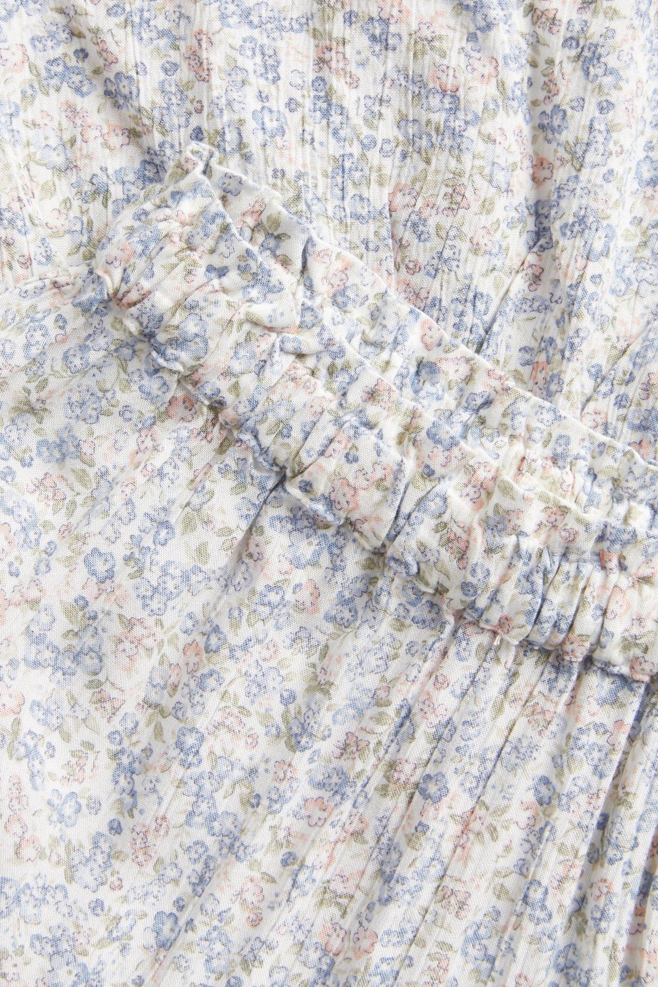 Zbliżenie na kremową spódnicę maxi w drobne kwiatki, z niebieskimi i różowymi kwiatami oraz falbanką.