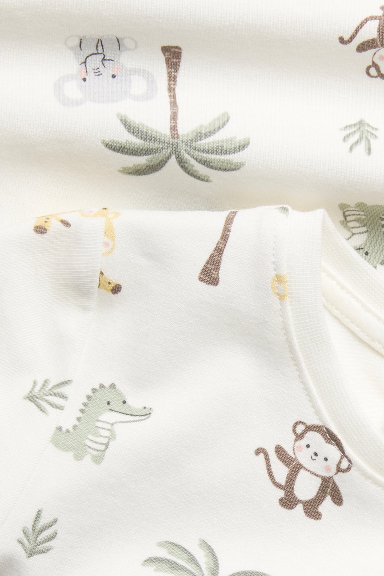 Nærbilde av en offwhite kortermet babybody med fargerikt jungeldyrmønster og trykknapper ved skulder.