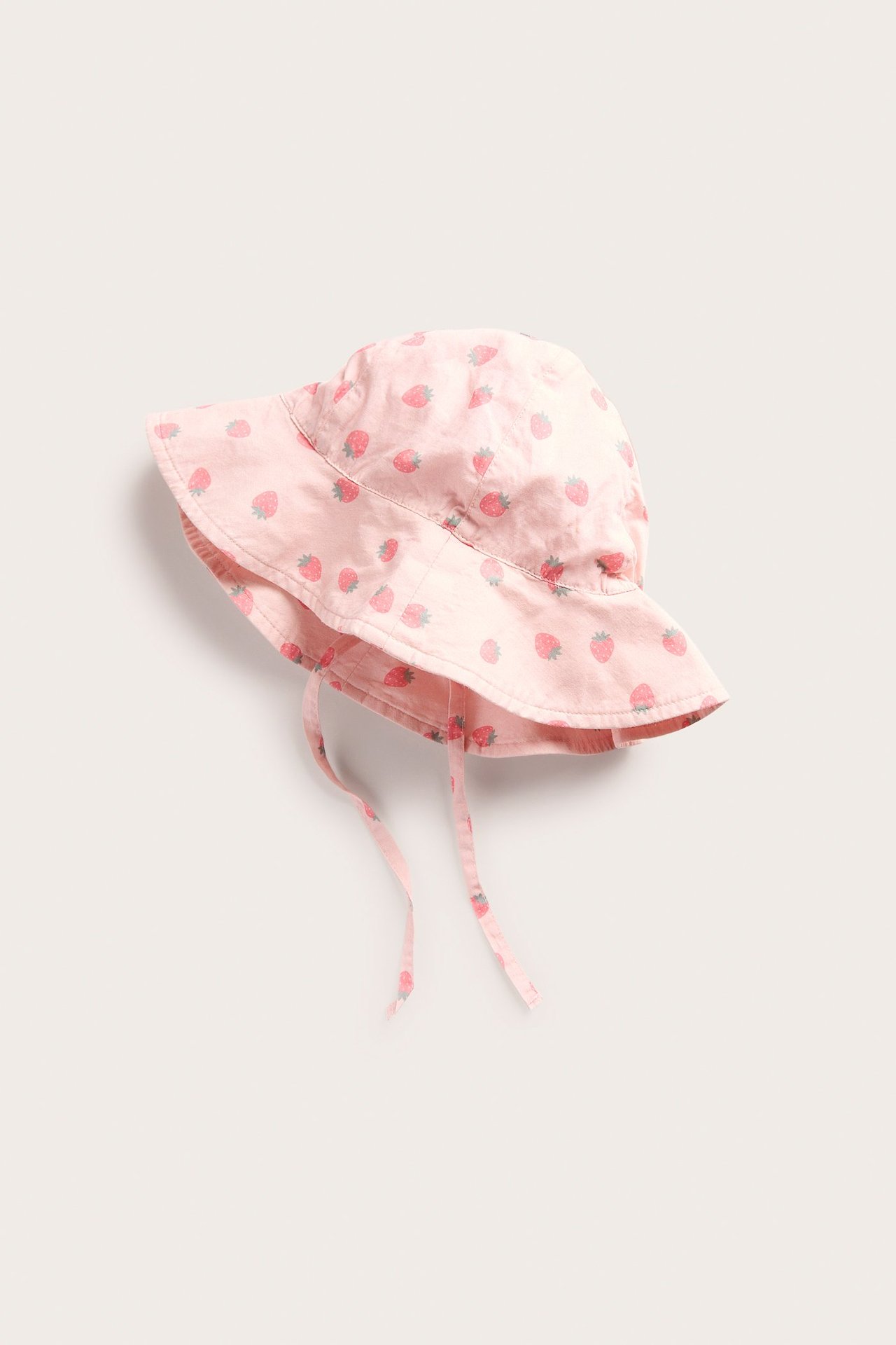 Framifrån, en baby ljusrosa vävd solhatt med jordgubbsmönster och knytband.