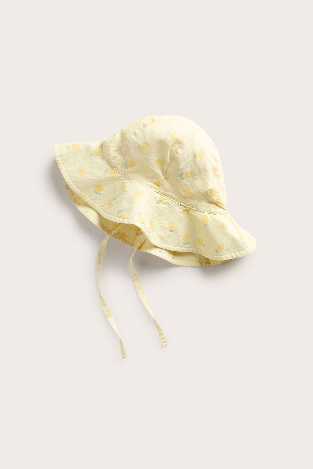 Ovenfra sett en baby lys gul vevd solhatt med sitronmønster og knytebånd.